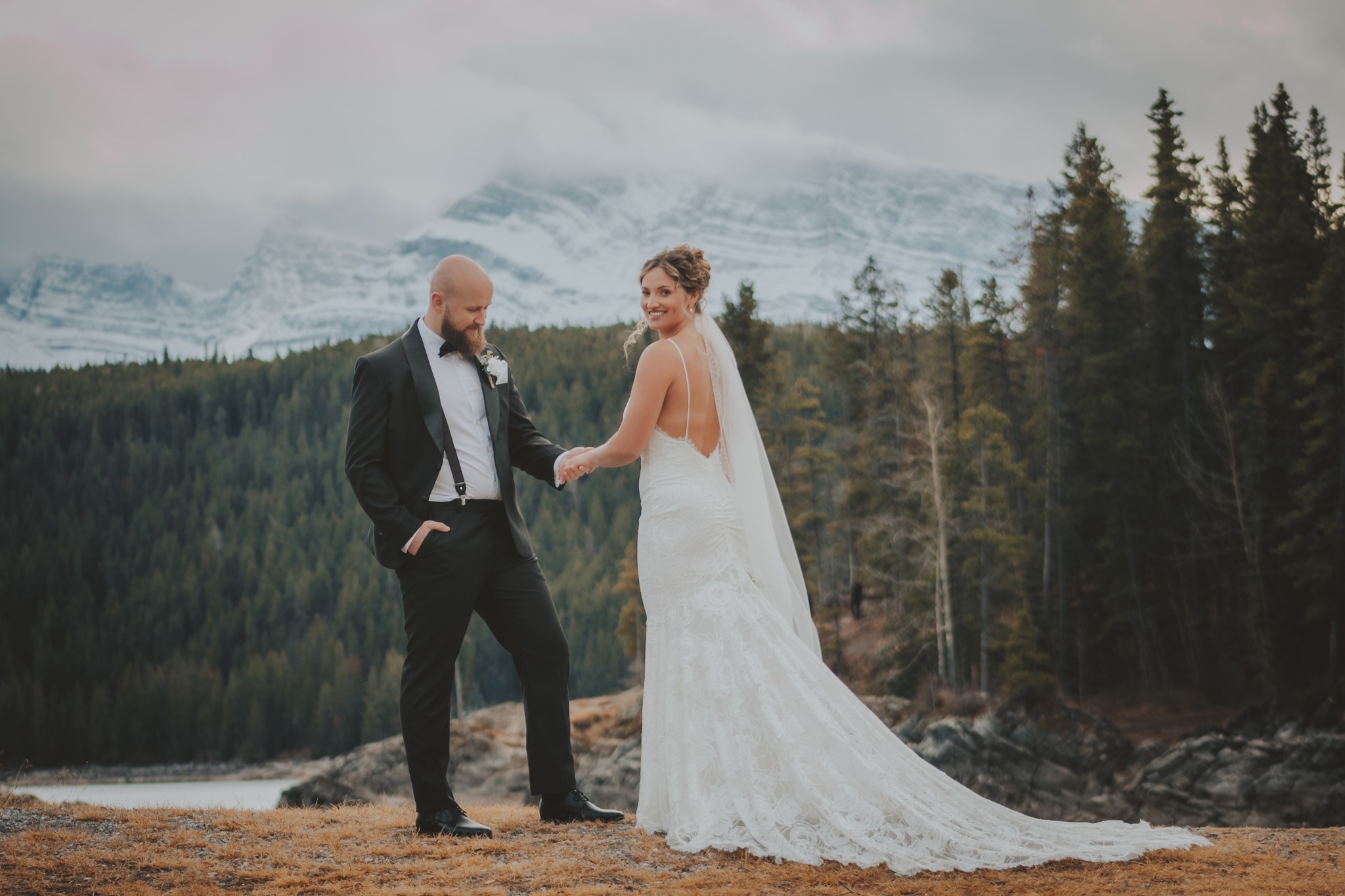 Bride and groom standing hand-in-hand on a grassy overlook