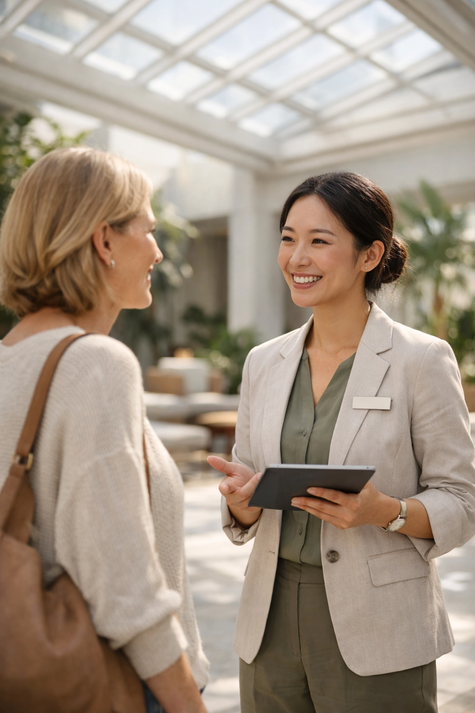 Hotel staff using a tablet to provide personalized guest service in a bright modern hotel atrium.