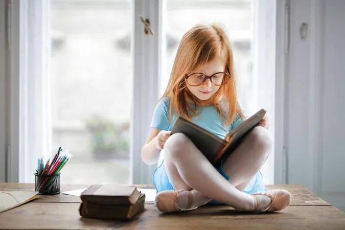 A young girl with glasses deeply focused on her reading, reflecting the confidence built through mastered skills.
