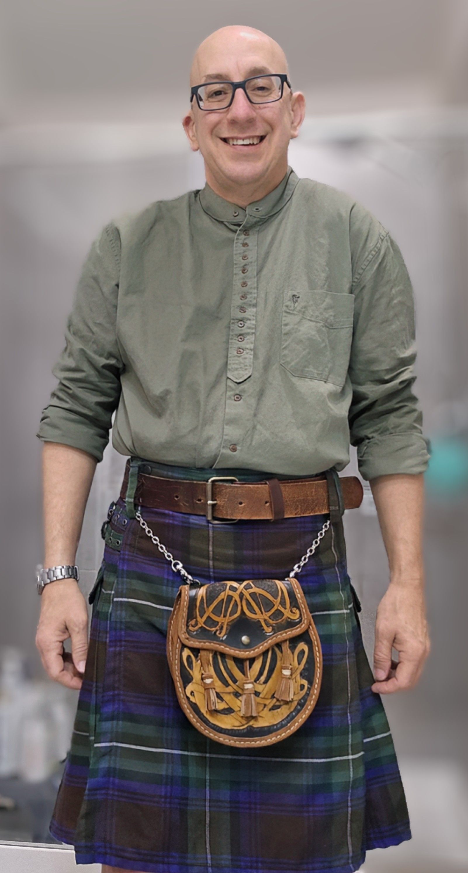Eric wearing a green shirt and a kilt with a sporran, smiling.