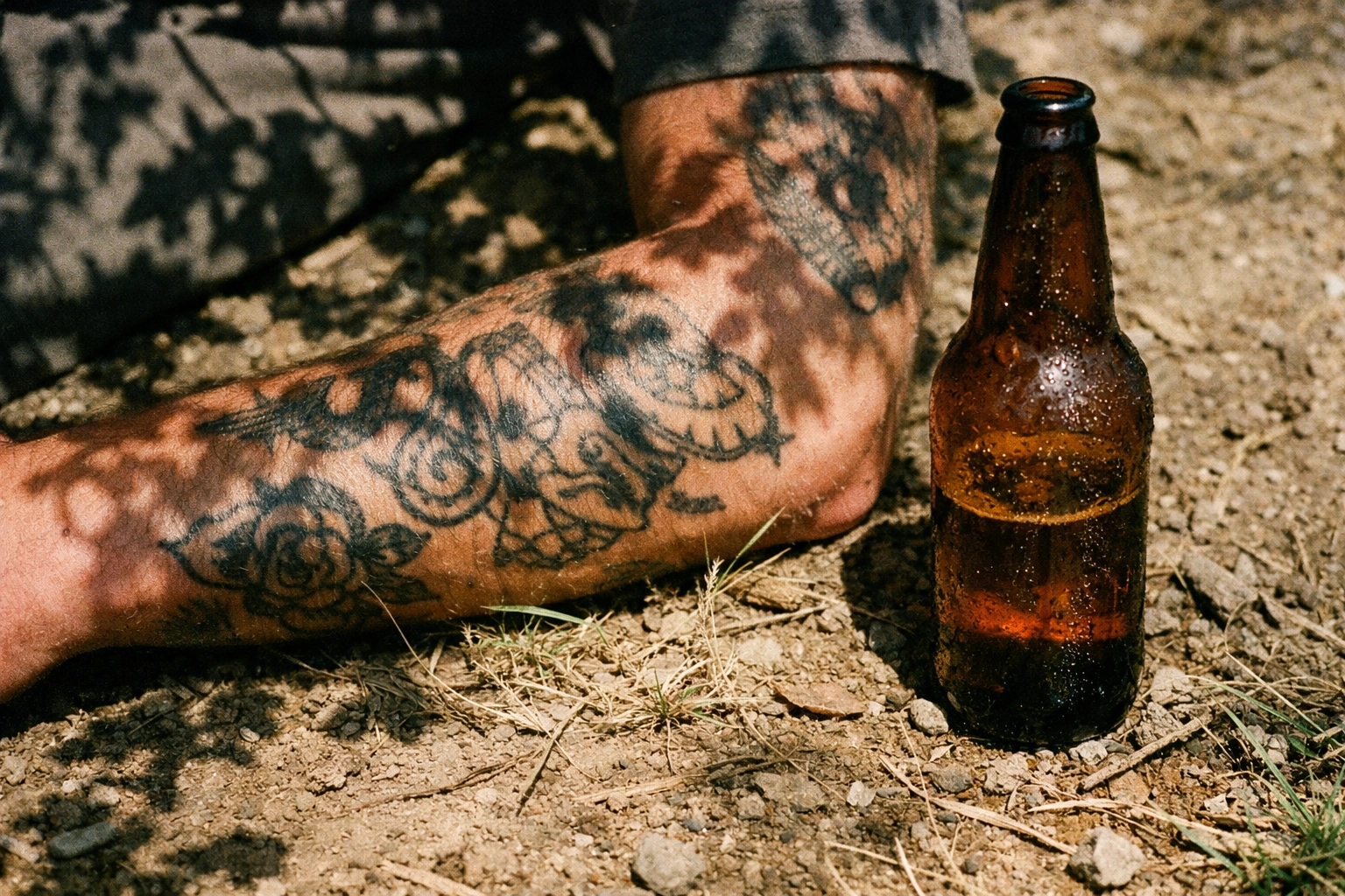 A tattooed arm and a beer bottle on the ground at Hasenheide FKK, Neukölln's naked park.