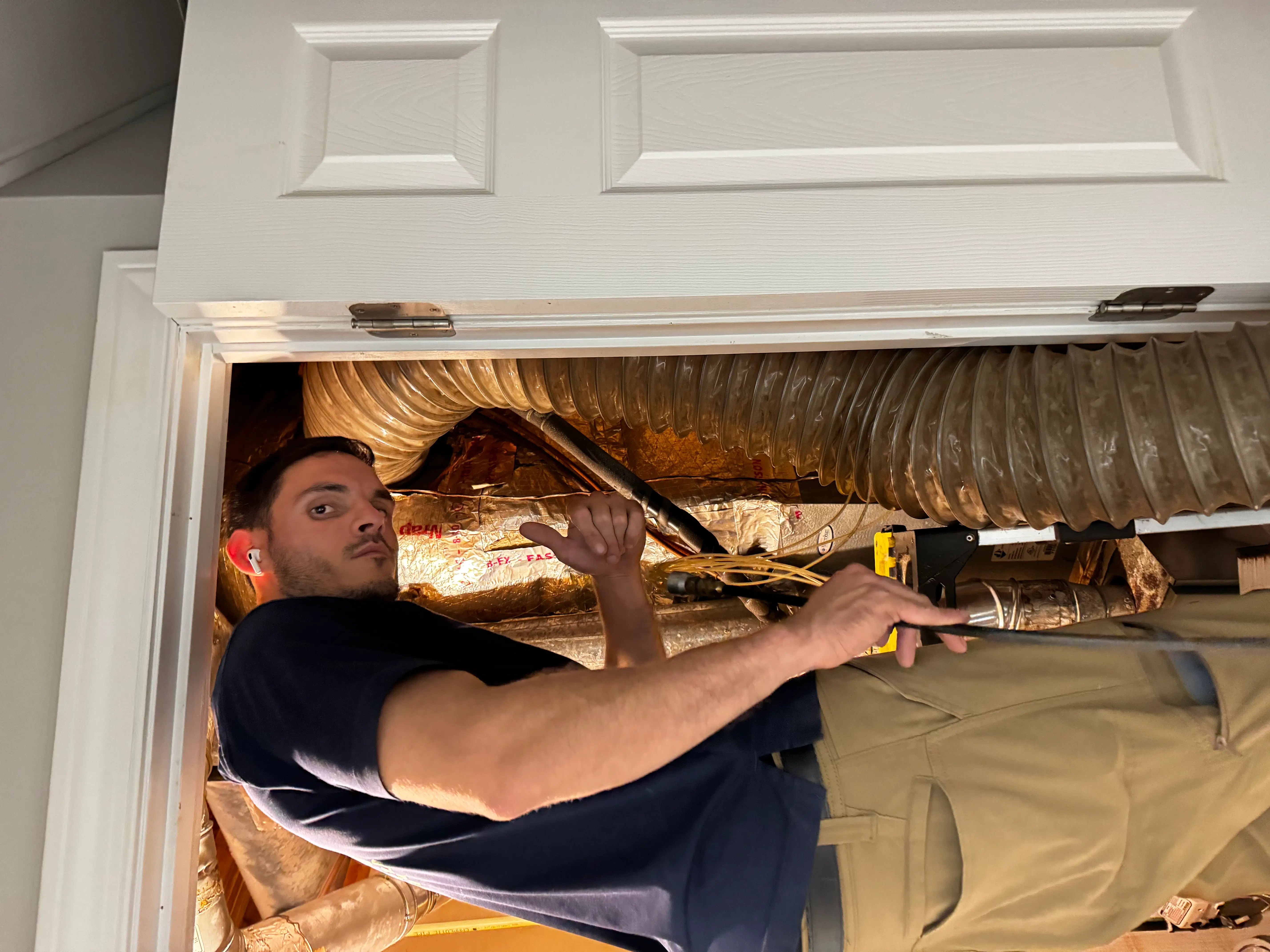LServices technician performing air duct inspection and cleaning preparation in an attic space