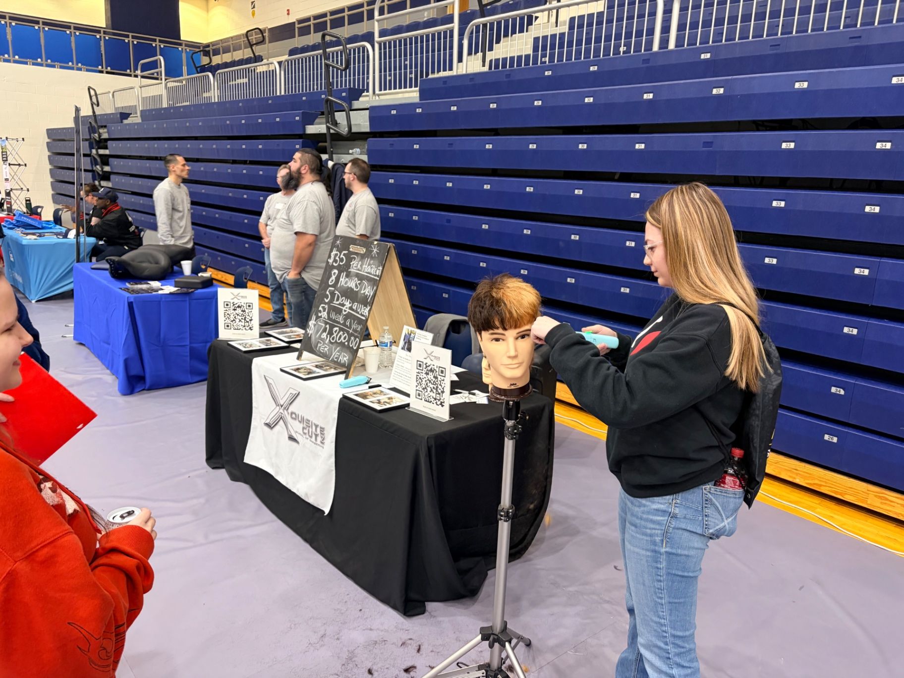 Hands-on student engagement at the X-Quisite Cutz career fair booth, career pathway discussion, barbering tools, supervised learning environment.