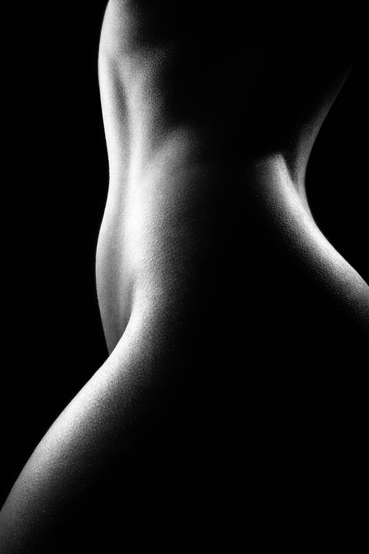 High-contrast black and white fine art nude photography emphasizing light and shadow on the hip and waist.