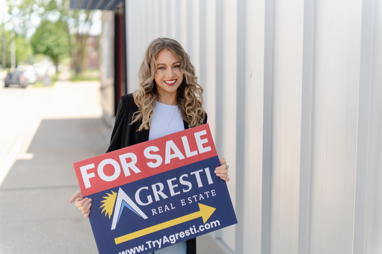 Smiling female real estate professional with For Sale sign