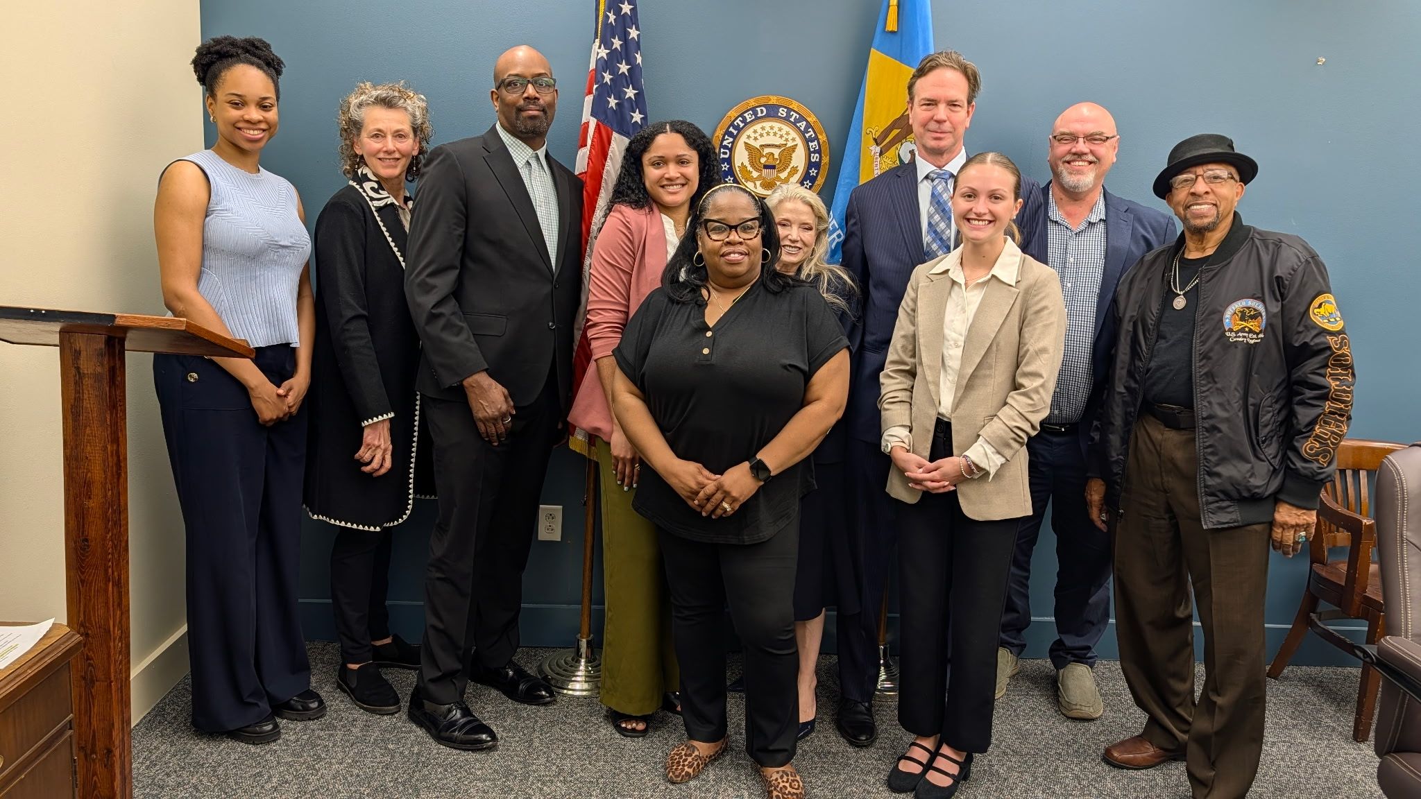 Ken-Do Spice meeting with Senator Coons’ staff, showing a diverse group of business professionals in front of American and Delaware state flags.