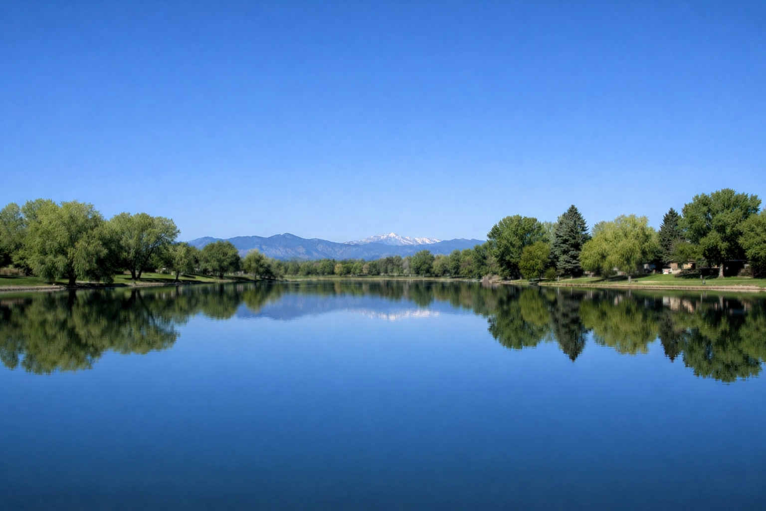 Scenic view of Harvey Park Lake in Denver under a blue sky with mountain foothills in the distance.