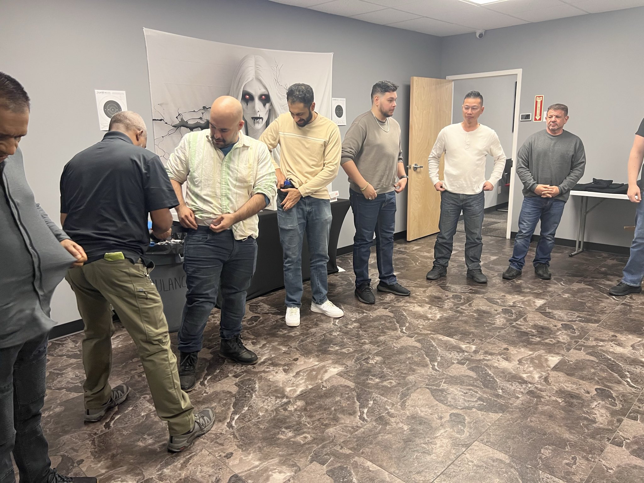 Instructor demonstrates proper concealed carry techniques to a group of adult students during a handgun safety training class at C&G Solutions. Participants practice drawing from holsters in a classroom environment as part of the NY State 18 hour Conceal Carry Course.