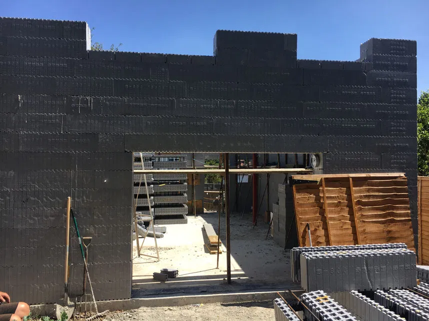 icf-block-wall-construction.webp A residential building under construction using insulated concrete form (ICF) blocks, showcasing the structural wall and large doorway opening.