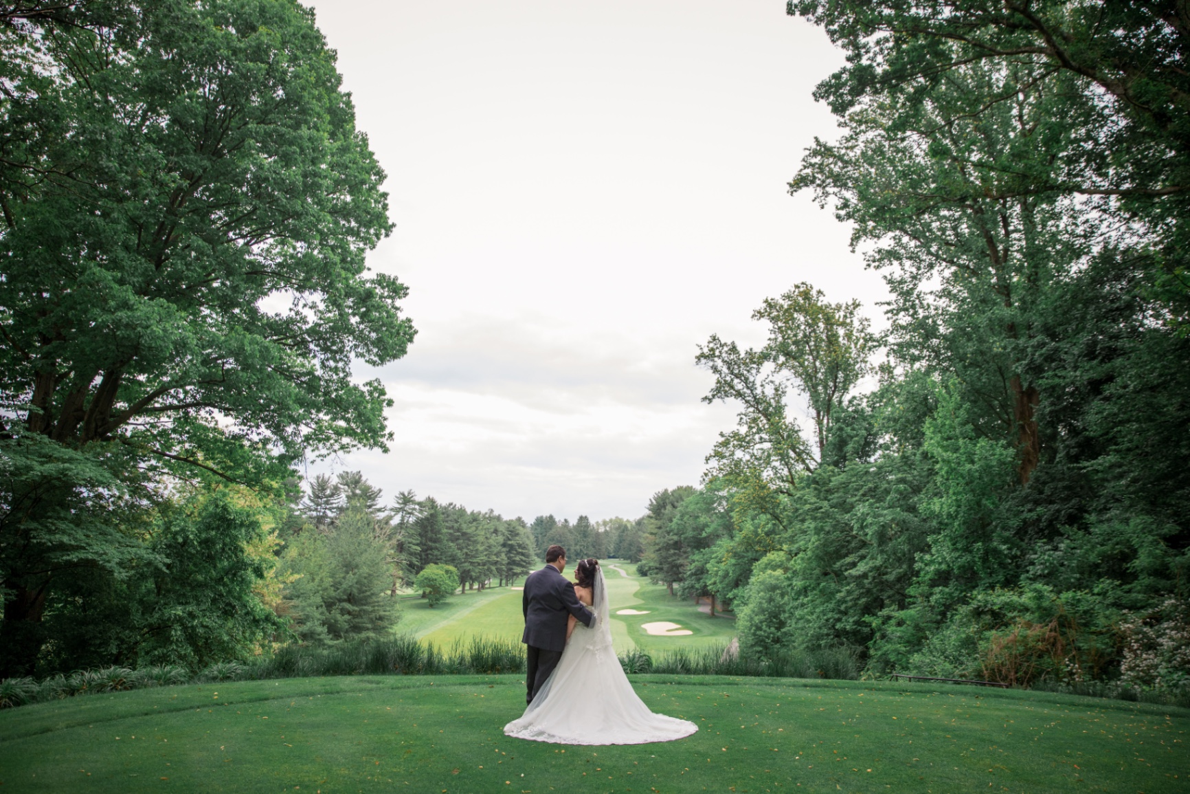 Bride and groom stand arm in arm on the golf course, gazing out over the greens