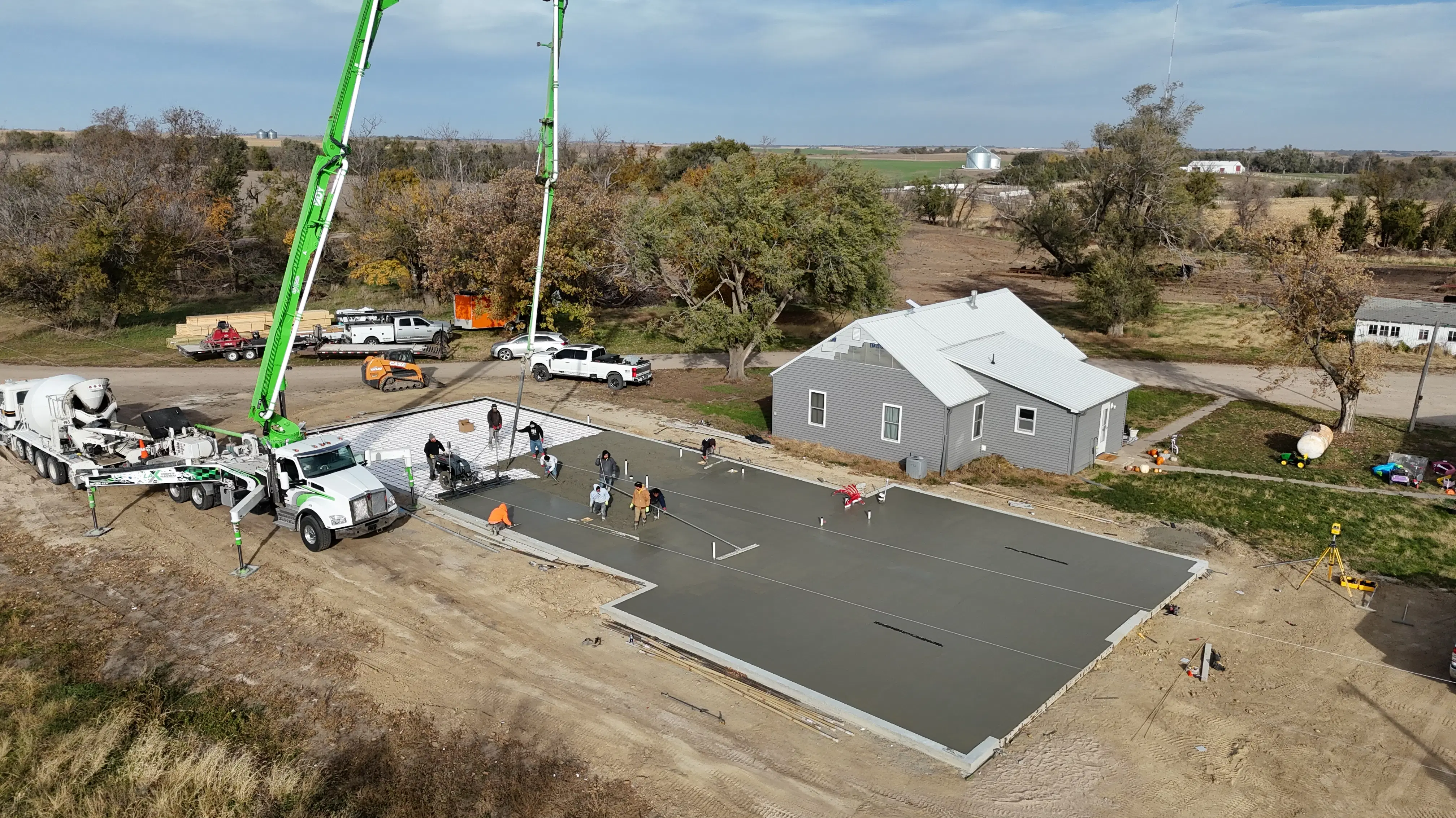 A crew from H&H Concrete and Construction pours and finishes a large residential concrete slab foundation using a concrete pump truck.