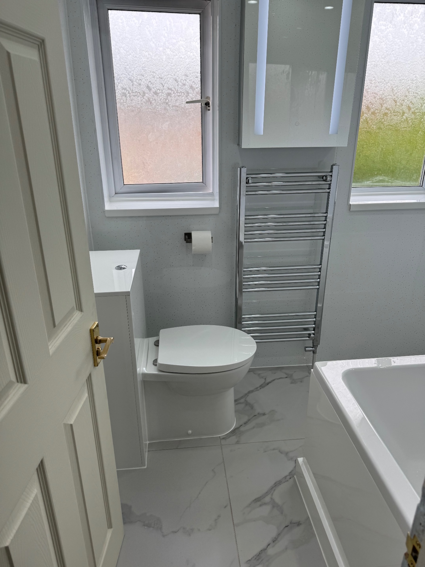 Modern, eco-friendly bathroom installation featuring a sleek white toilet, built-in cistern, and heated chrome towel rail.