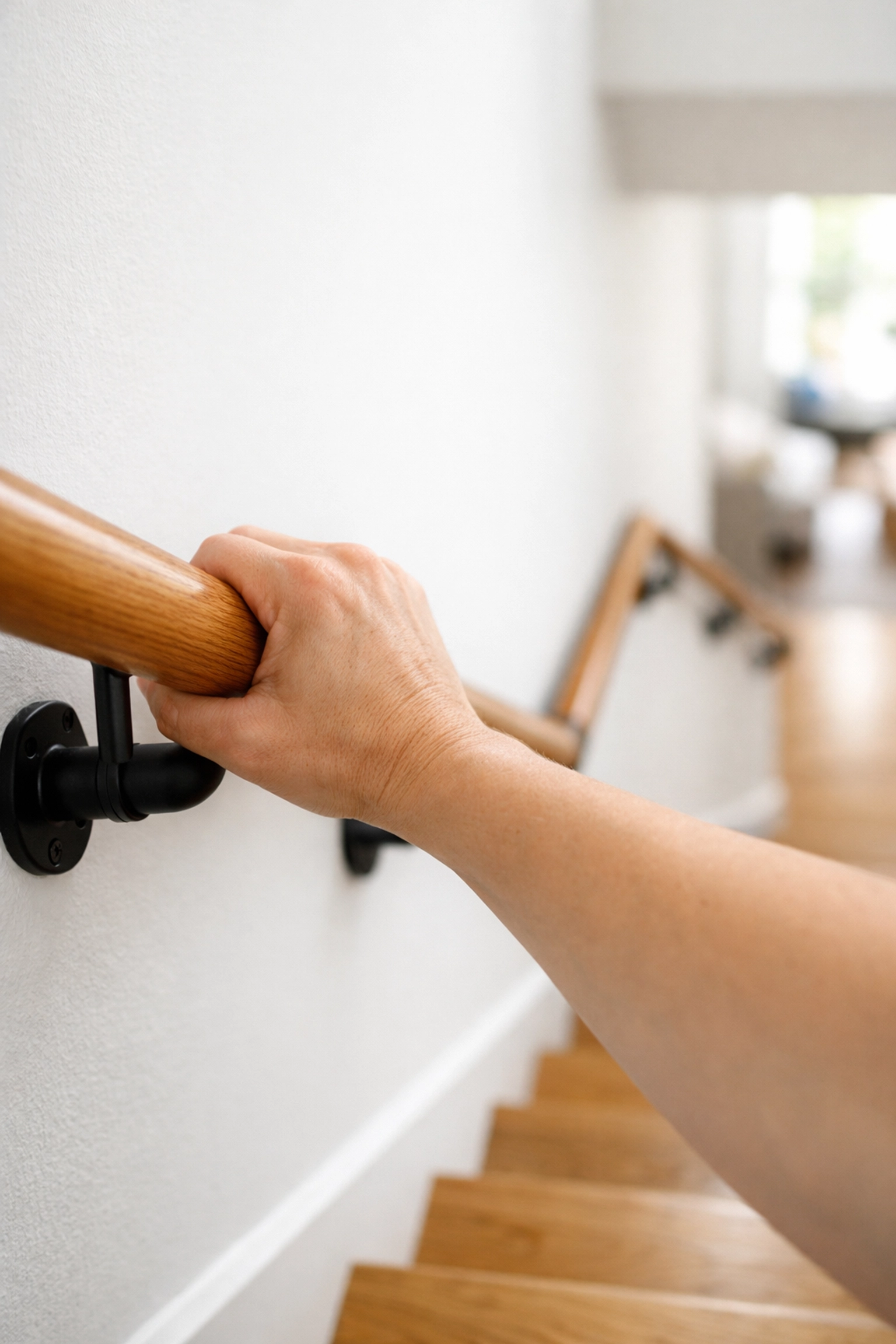 A person’s hand using a sturdy wooden handrail for stability while navigating home stairs.