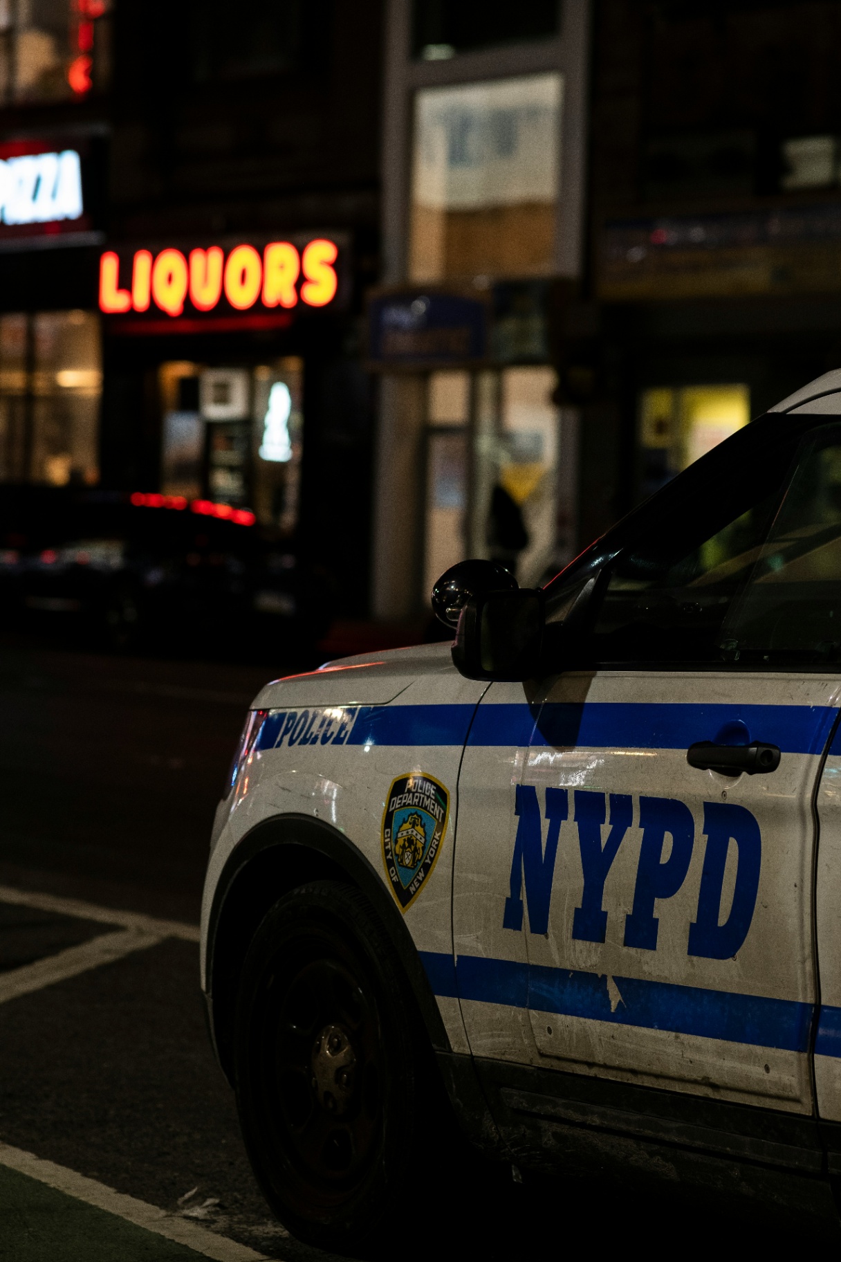 A marked NYPD patrol vehicle is parked on a city street at night