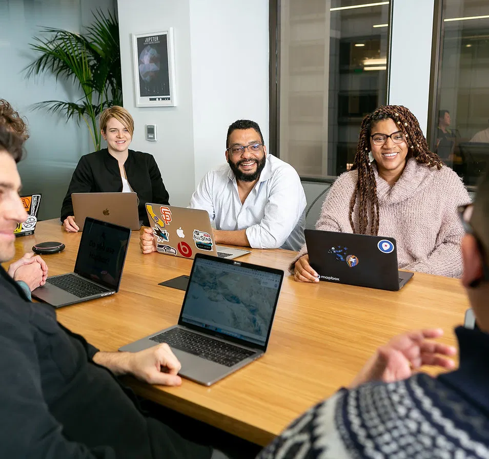 A diverse digital marketing team engaged in a collaborative meeting around a conference table, each member using laptops.