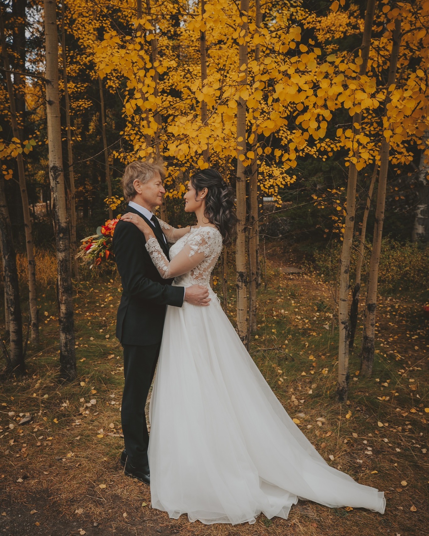 A couple stands embracing in a forest of golden aspen trees