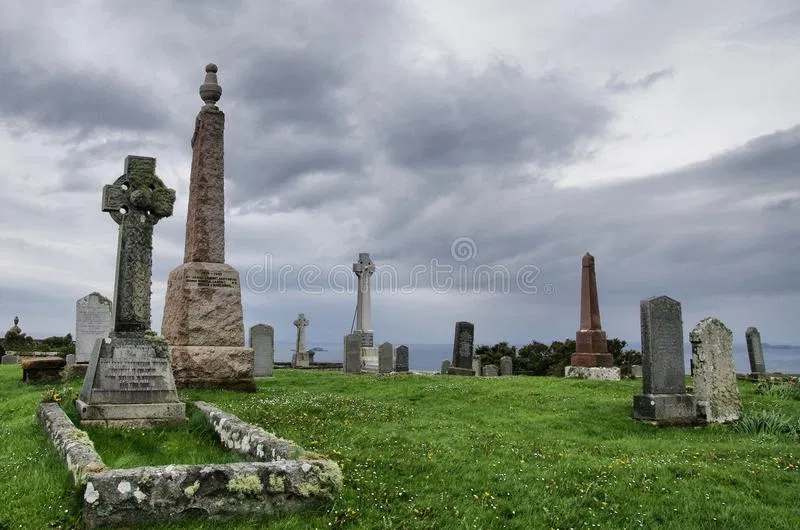 Overcast sky above a historic Scottish cemetery featuring weathered gravestones, Celtic crosses, and tall stone monuments