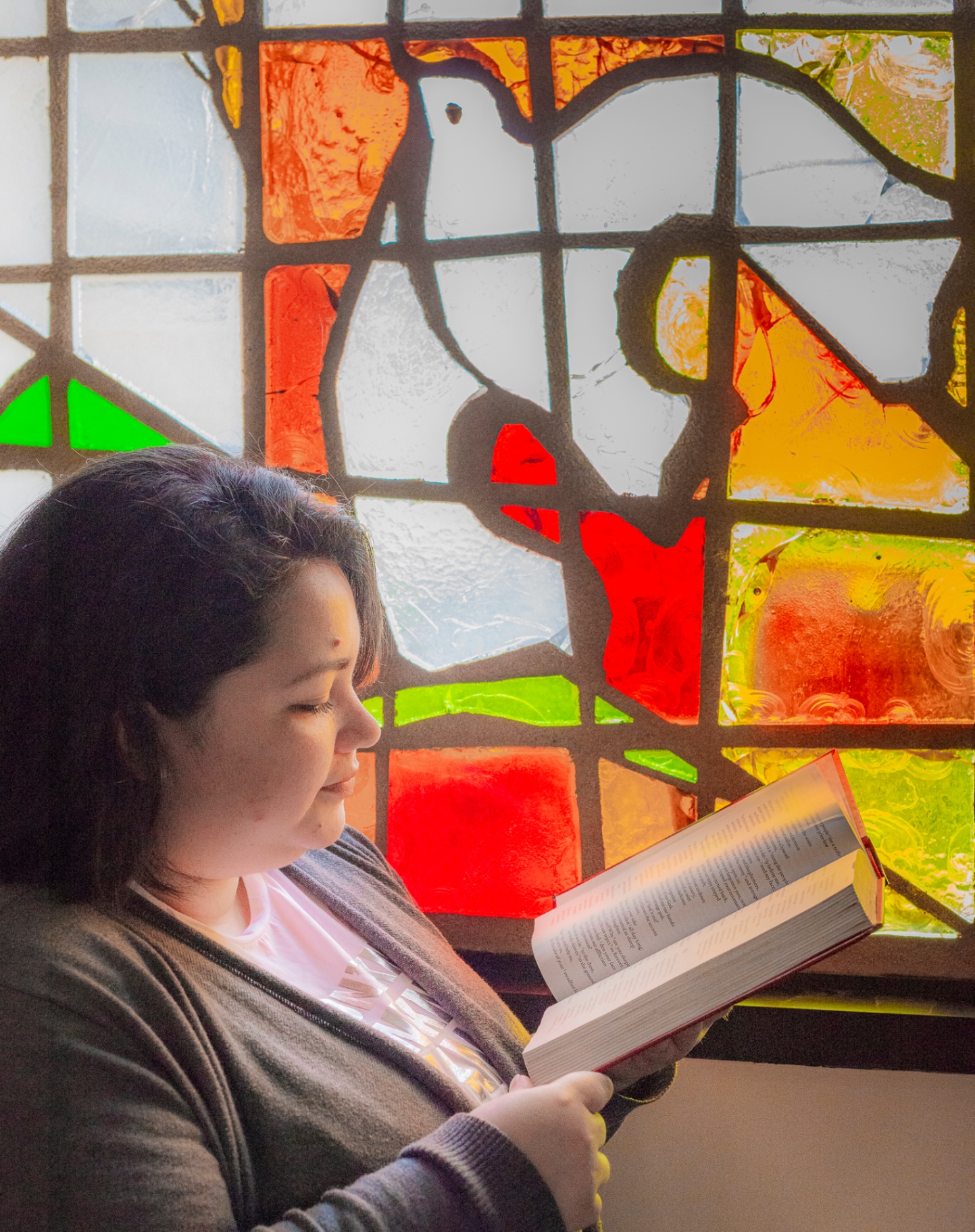 A student studies scripture beside a vibrant stained-glass window