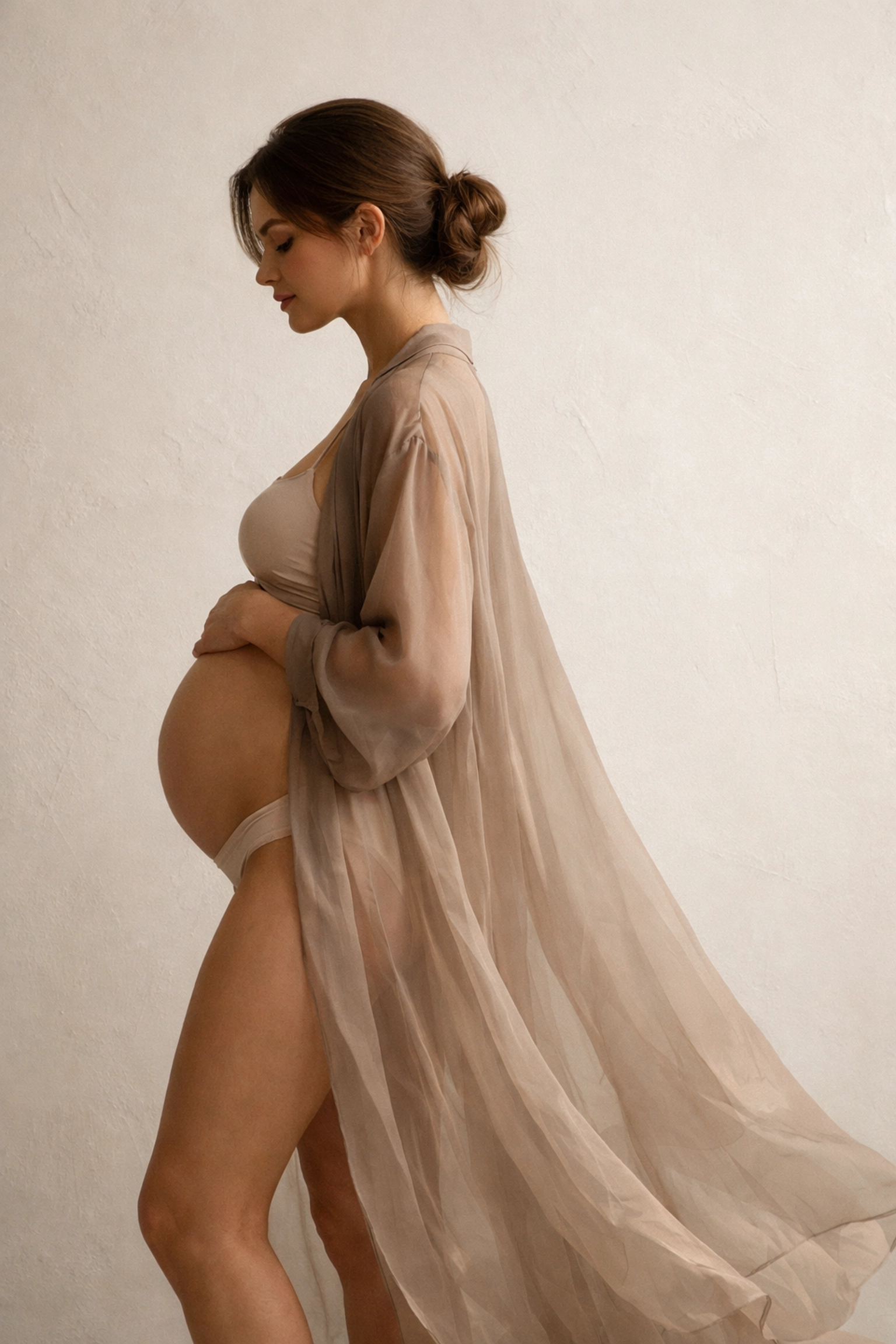 Elegant studio maternity portrait of a pregnant woman in a flowing silk duster with natural lighting.