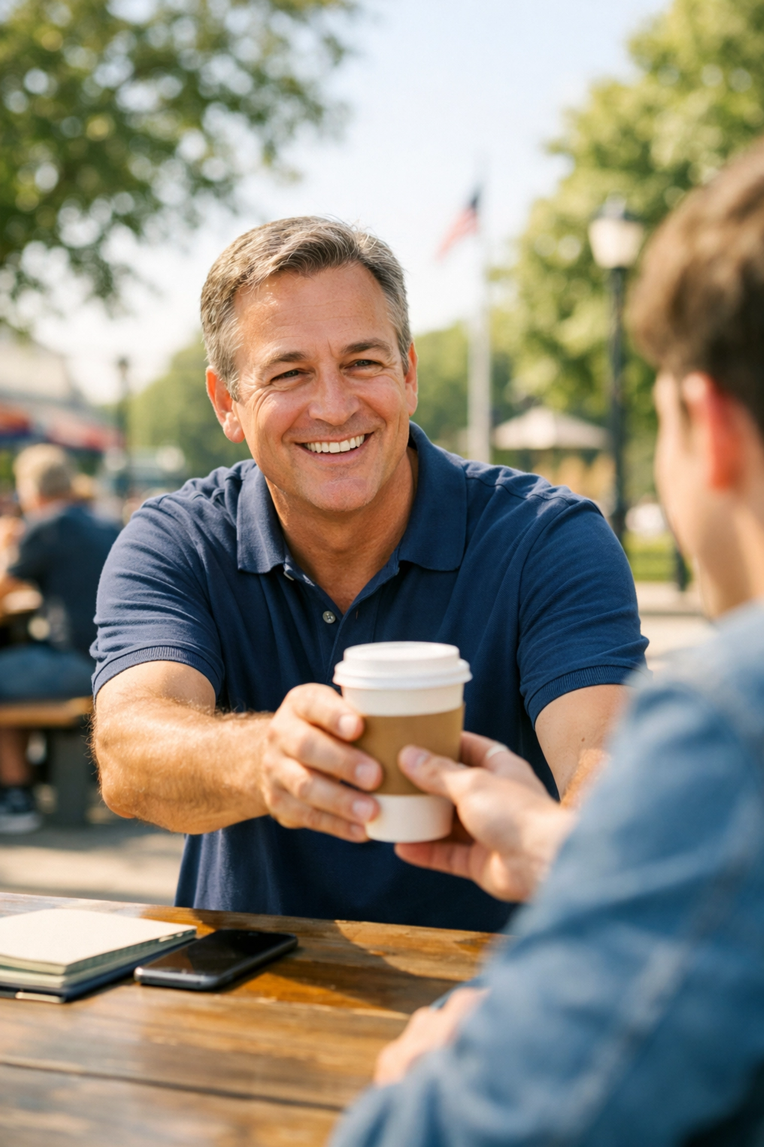 A CEO practicing civic values by sharing coffee with a community member in a sunny park.