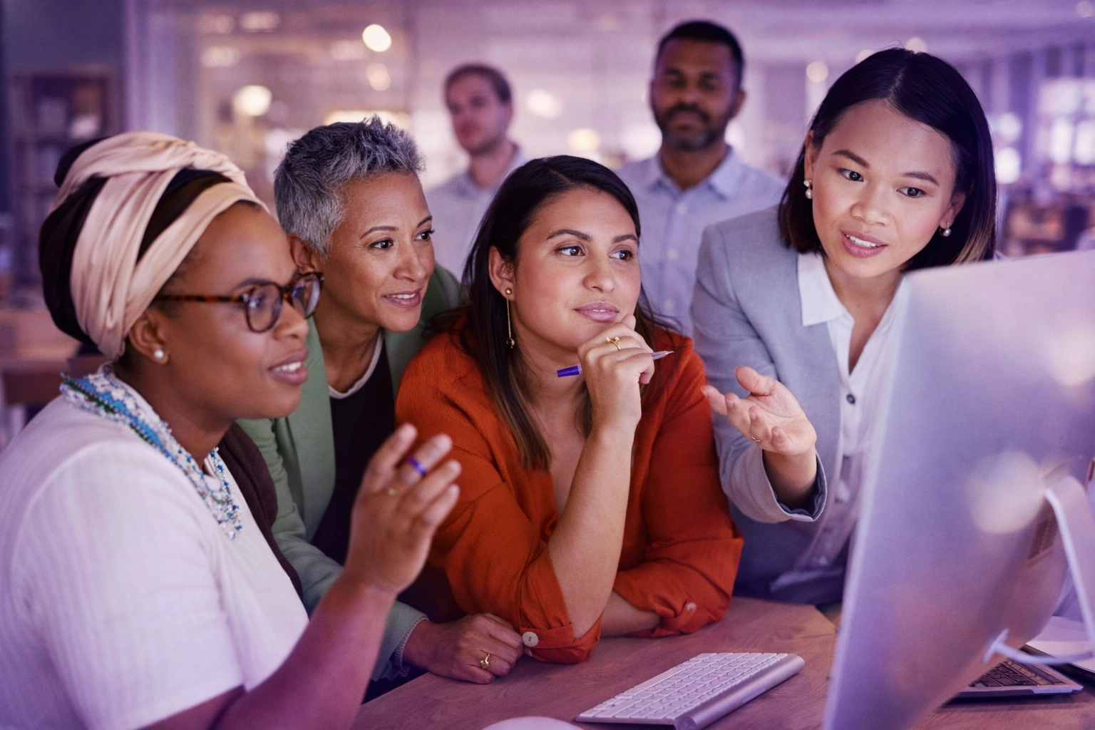 Diverse women of color team collaborating at a computer in a modern office, women leading the discussion, natural lighting with subtle purple tones