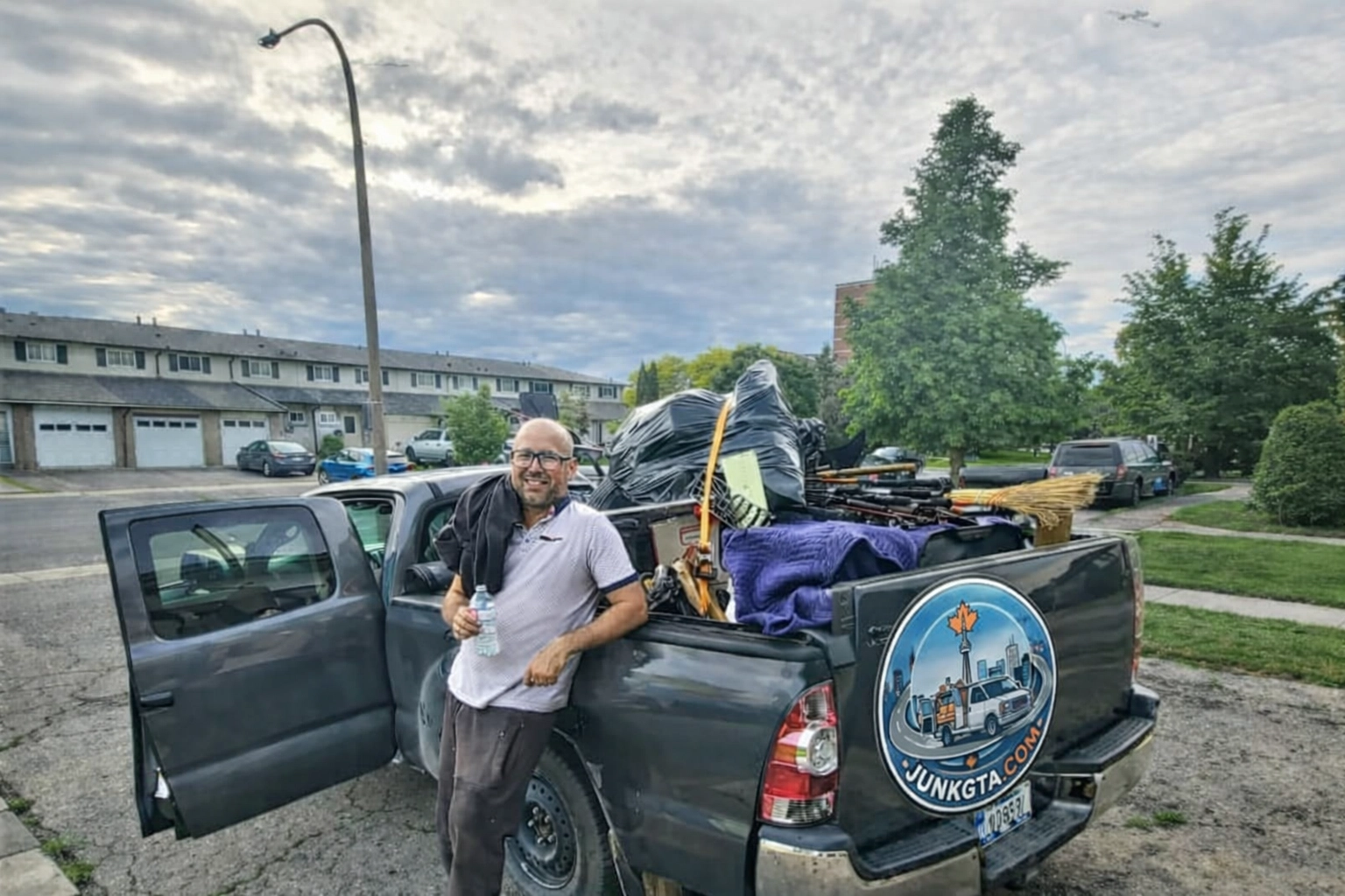 What Can I Put in a Construction Debris Removal Bin? Roman, owner of Junk GTA, standing by his 2014 Toyota Tacoma loaded with junk for removal in a residential neighborhood.
