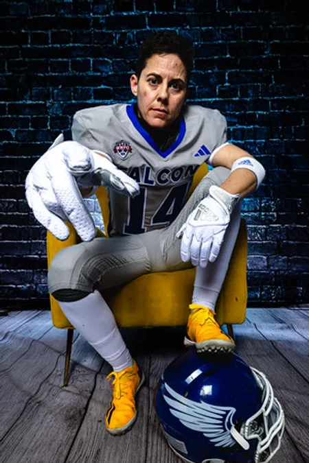 A football player in a full uniform sitting confidently in a yellow chair during a professional Media Day session.