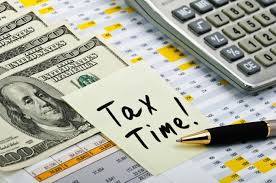 Tax Time Essentials A calculator, a stack of cash, tax documents, a pen, and a sticky note reading 'Tax Time!' emphasize the importance of timely tax preparation and filing services provided by Brick Taxes llc for both individuals and businesses.