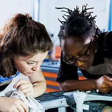 Two diverse students closely examine and work on a mechanical project together, demonstrating equity-centered, real-world STEM learning and collaborative problem-solving.