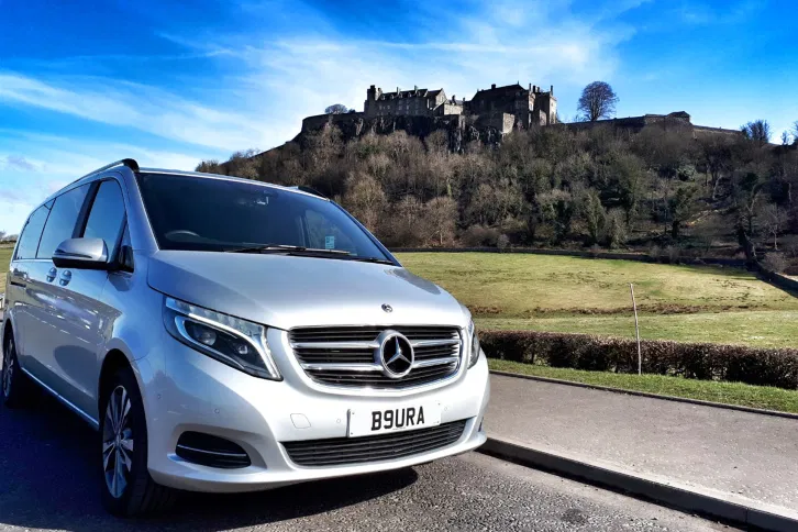 A luxury Mercedes-Benz chauffeur vehicle parked near a historic castle