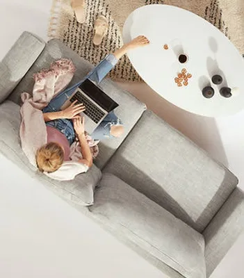 A client relaxes on a modern light-gray sofa, working comfortably from a laptop in a bright living room.