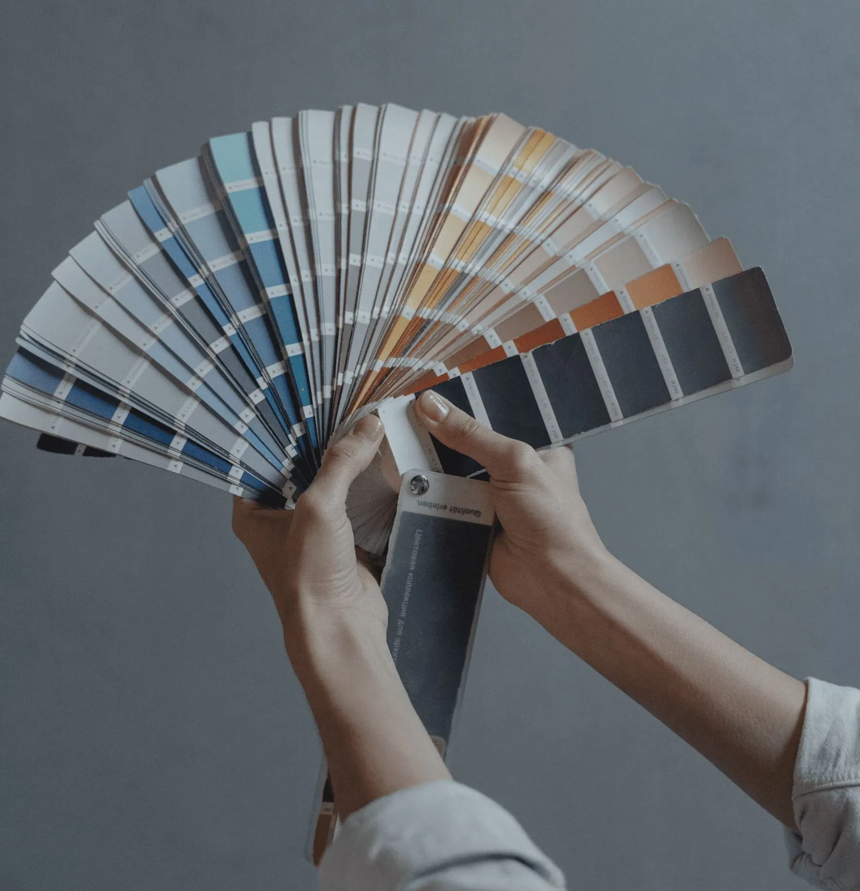 A person holds an extensive fan deck of paint color swatches against a neutral wall