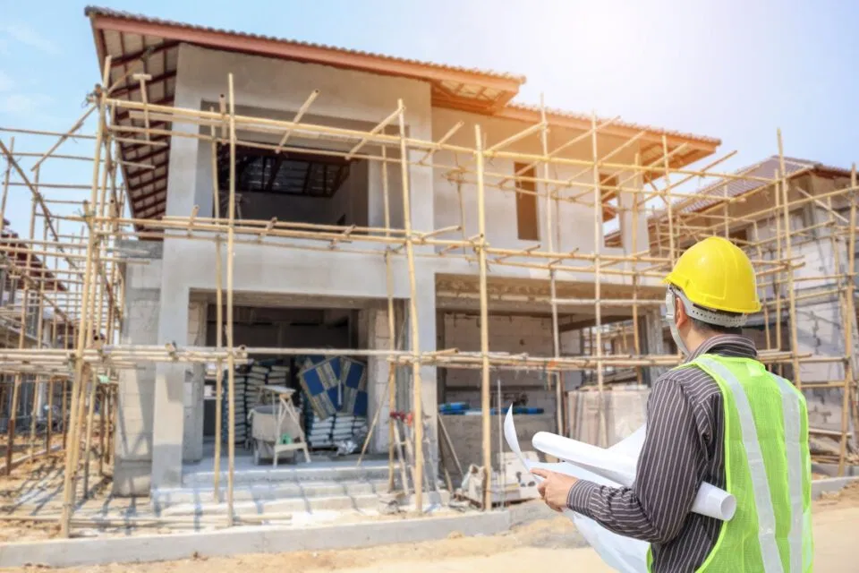 A construction project manager examines blueprints in front of a partially built structure, highlighting the massive demand for equipment financing in the building sector.