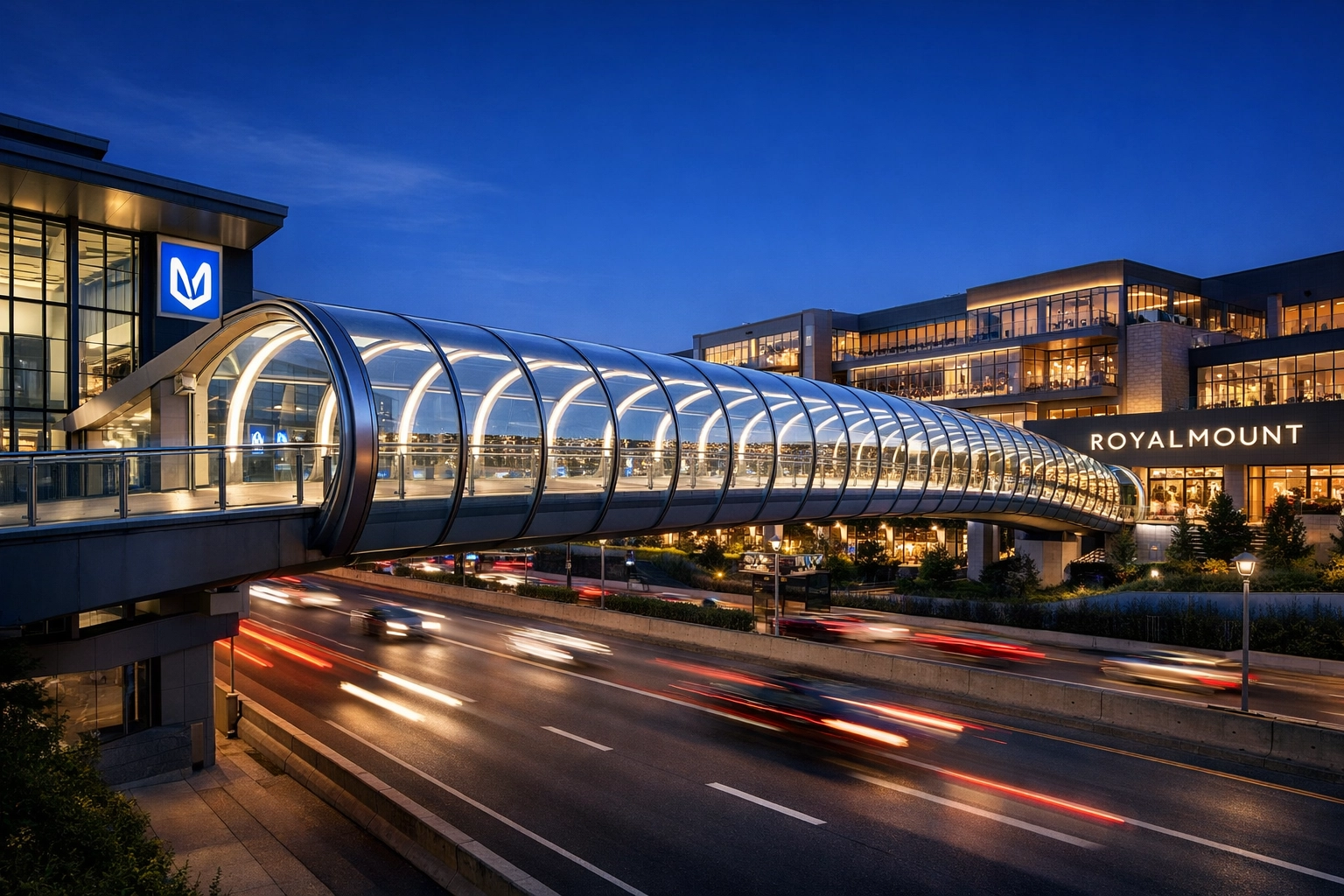 Modern glass pedestrian bridge at Royalmount Montreal lit up at dusk connecting to the metro station.