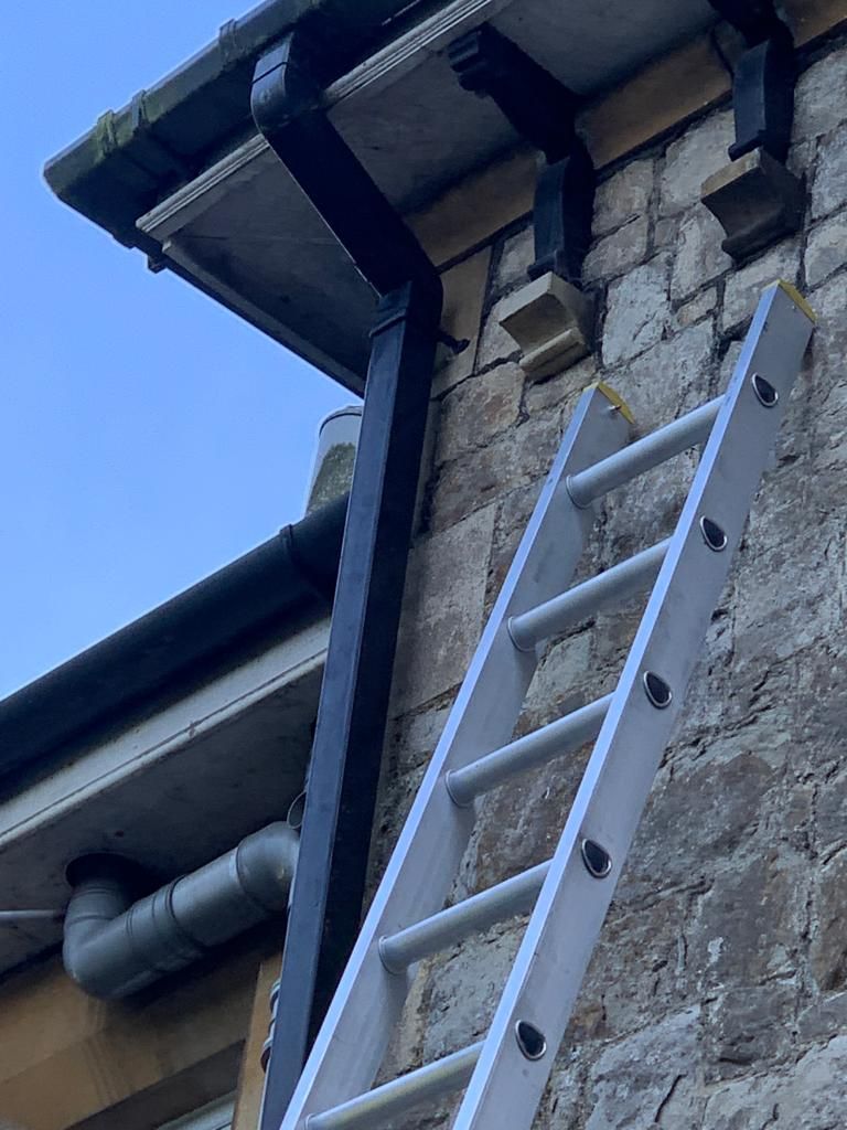 A ladder positioned against a building for manual gutter cleaning, showing the traditional access method.