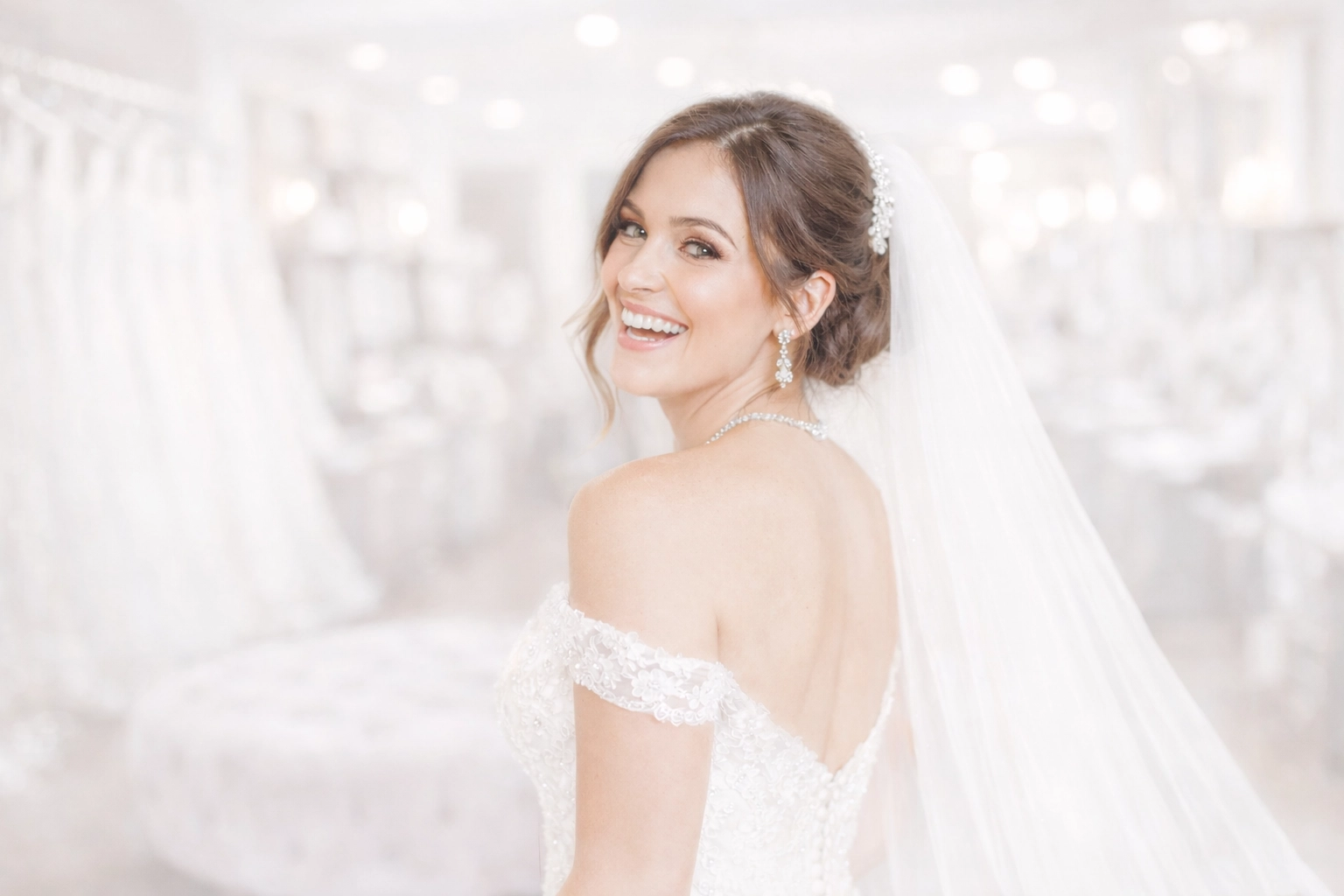 A fully accessorized bride wearing a cathedral veil and jewellery in a wedding boutique.