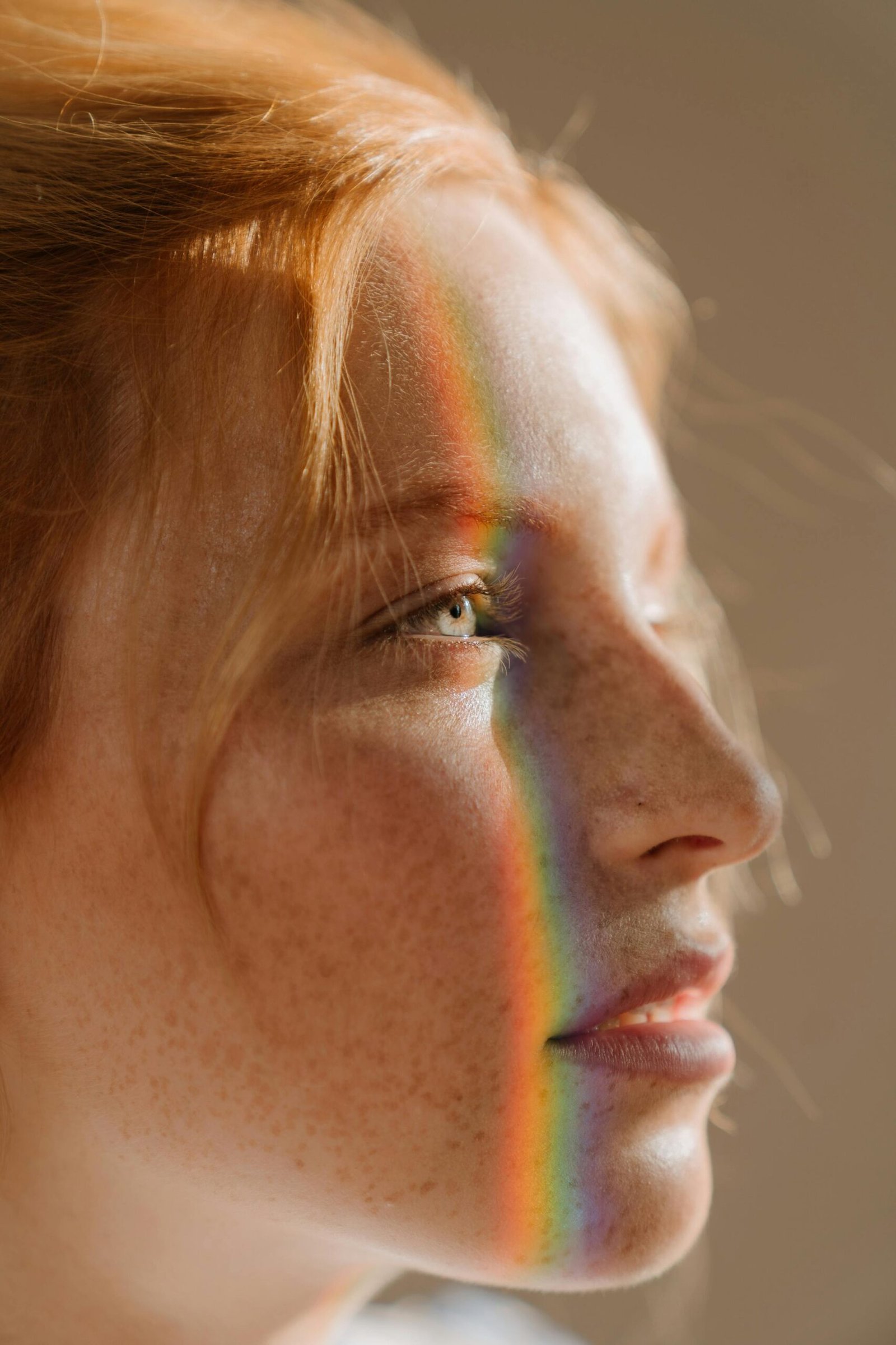 Close-up of a woman's freckled face with smooth, healthy-looking skin. A rainbow light reflection runs vertically across her face, highlighting natural beauty and skin texture: ideal visual for promoting AEtherbal's skincare and beauty products that enhance complexion and support radiant, healthy skin.