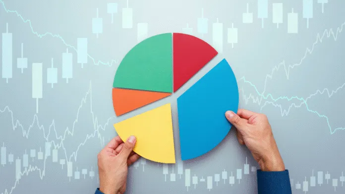 A person arranges segments of a colorful pie chart over a background of stock market candlestick charts and line graphs