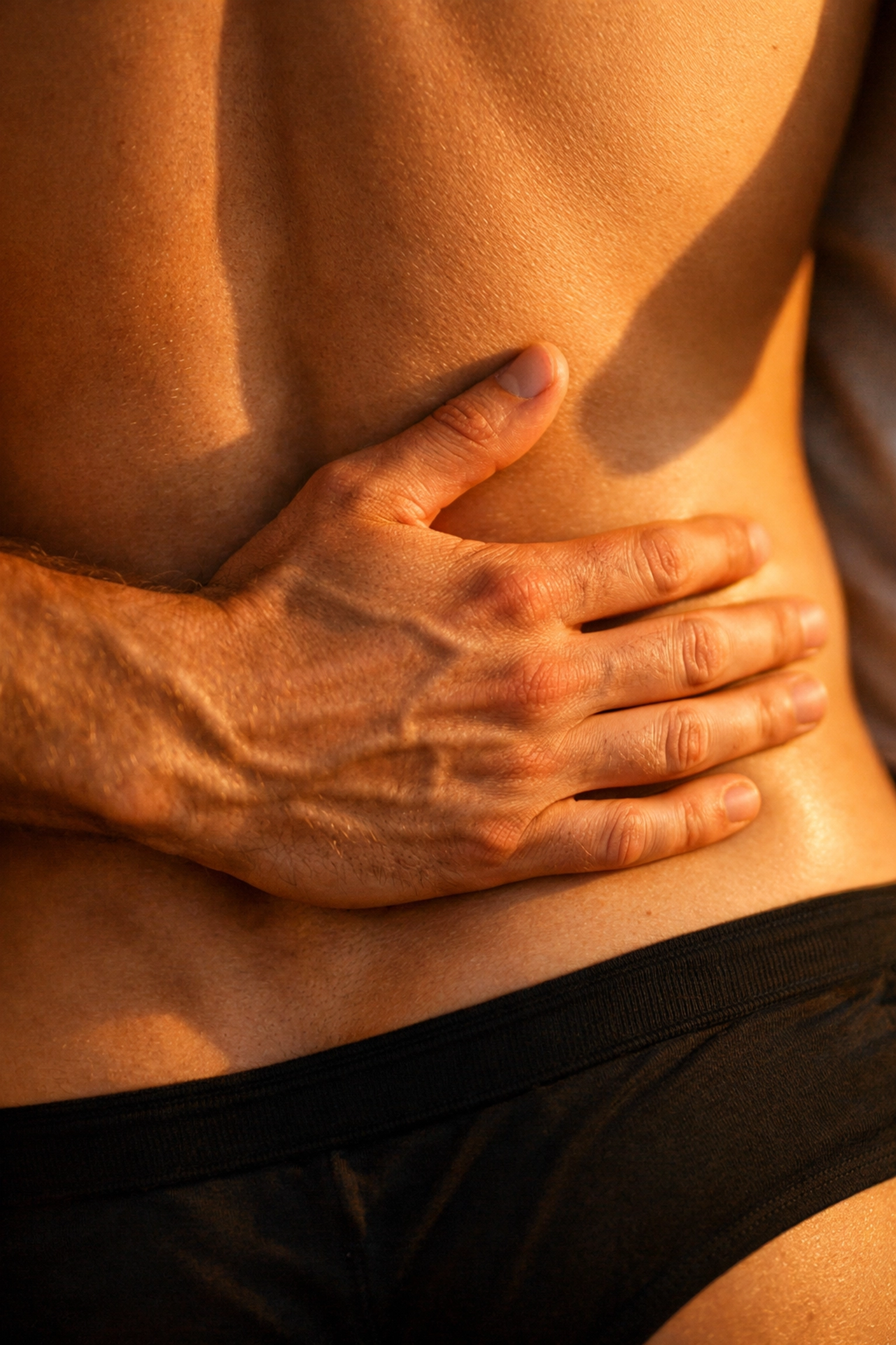Close-up of a hand resting on a man's muscular back, showcasing male muscle definition and intimate queer touch.