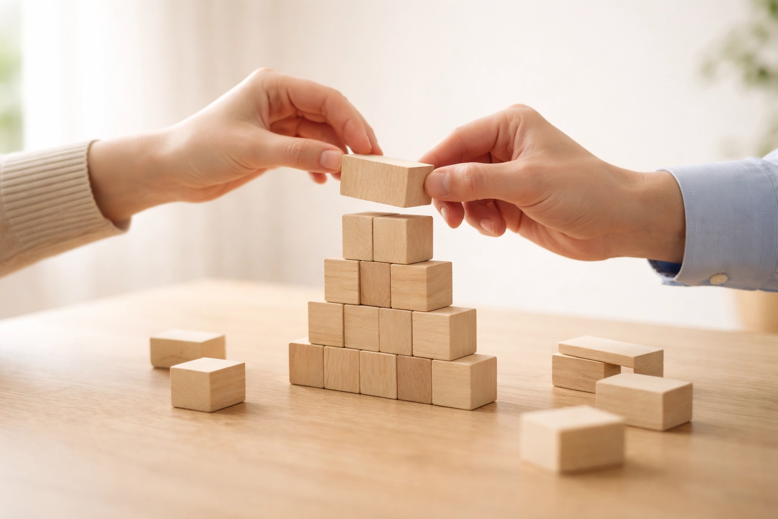 Two people building a wooden block tower together, illustrating teamwork and couples therapy progress.