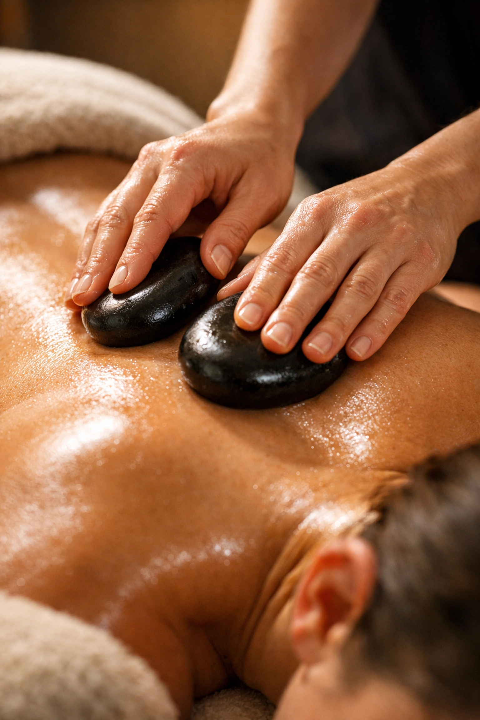 Massage therapist performing hot stone massage therapy on client's back
