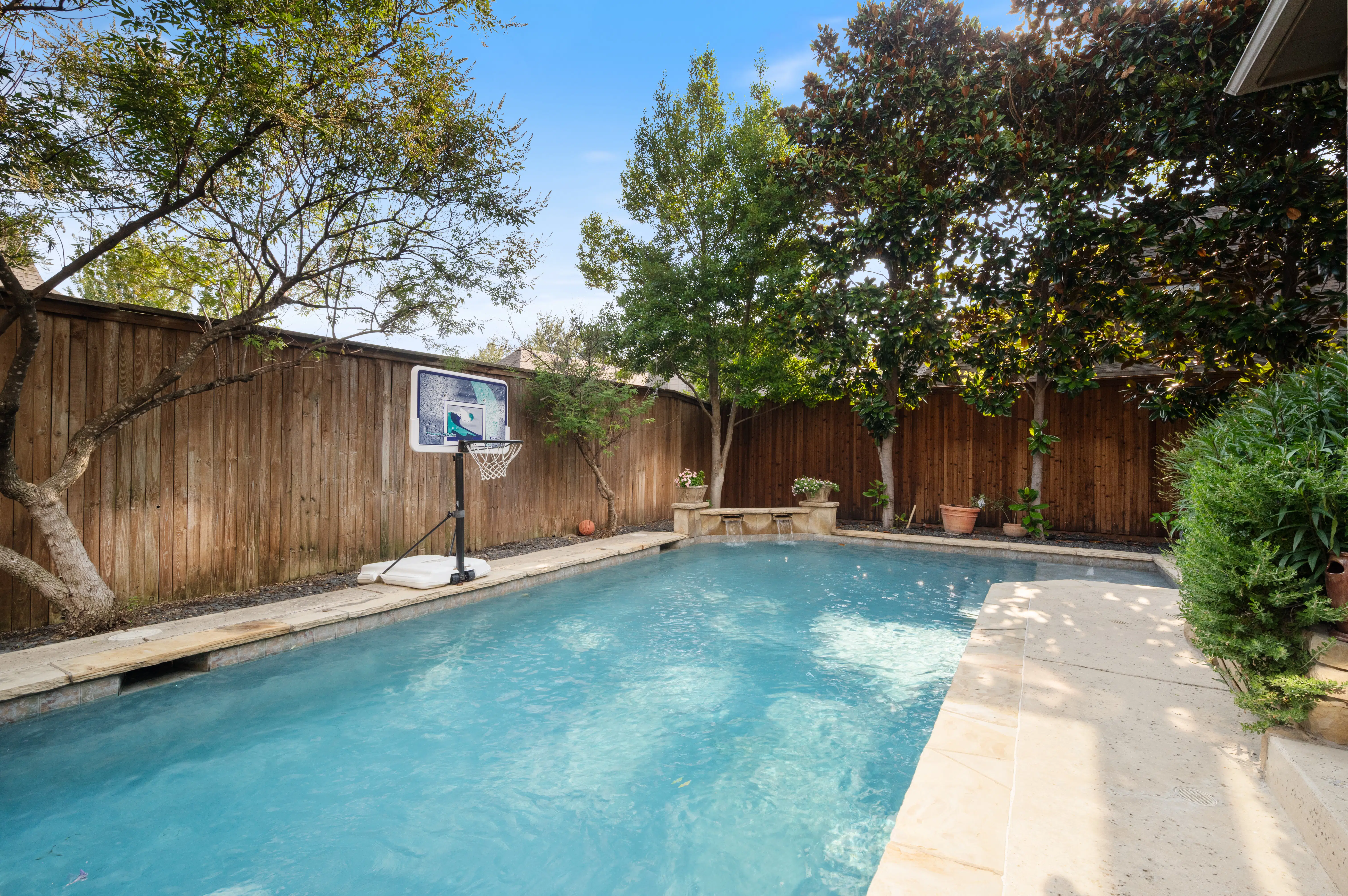 A private backyard oasis featuring a rectangular swimming pool with stone patio