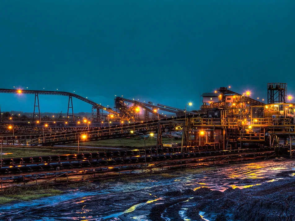 A brightly lit mining facility operating at dusk, conveying the scale and technical expertise required for complex industrial operations.