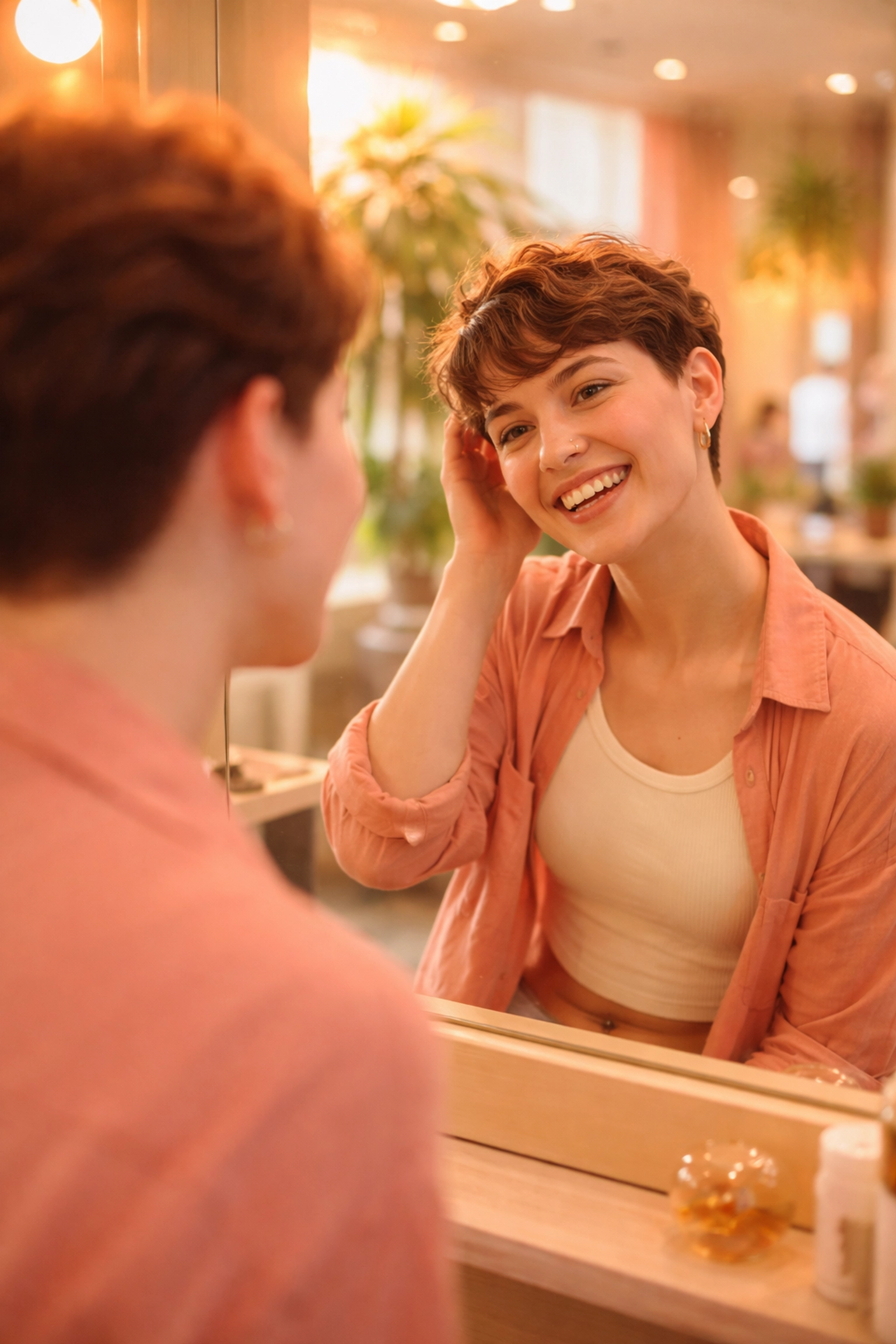 A joyful person smiles at their reflection in a salon mirror, celebrating a confident, gender-affirming haircut experience.
