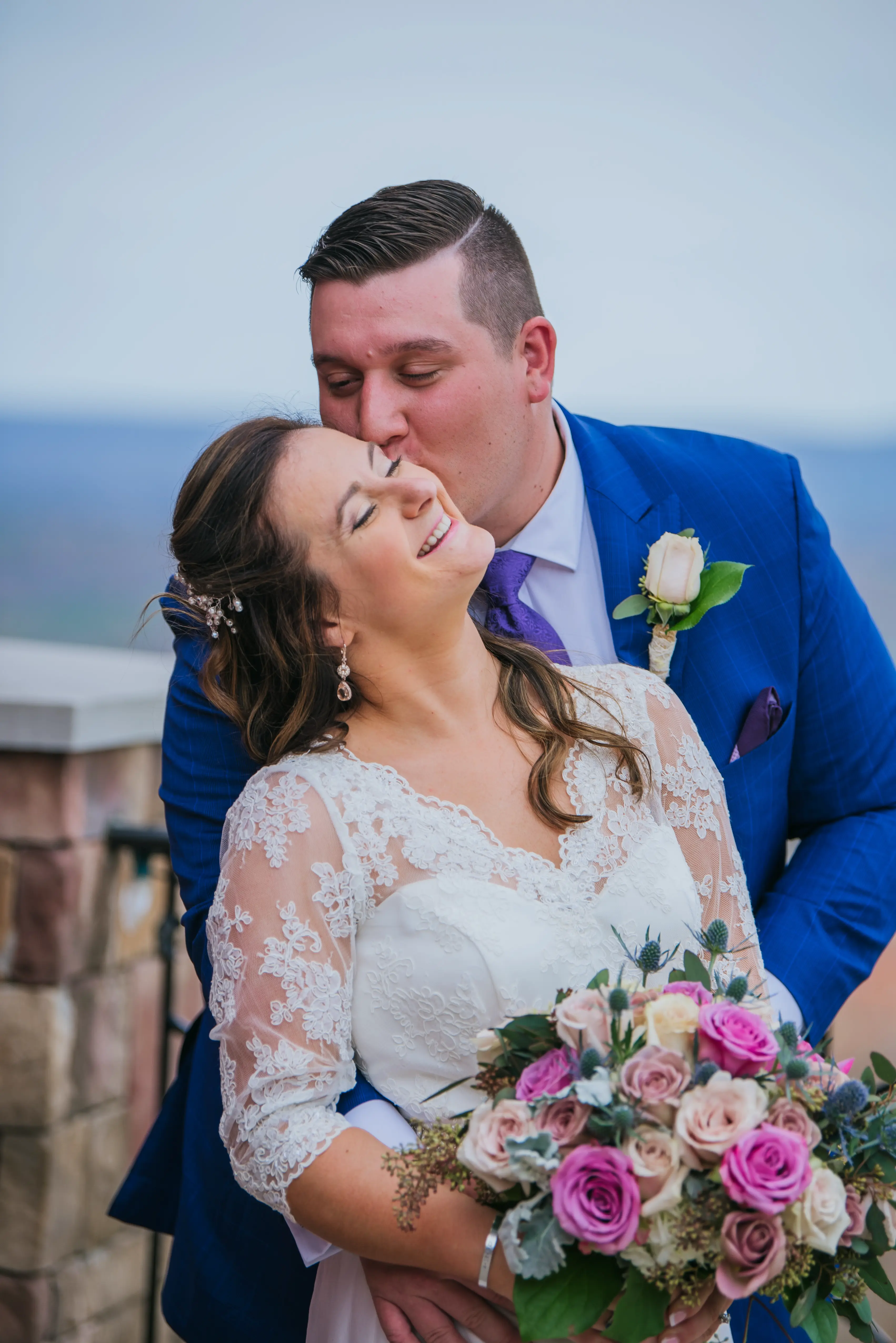 Groom in a blue suit tenderly kisses his bride on the temple