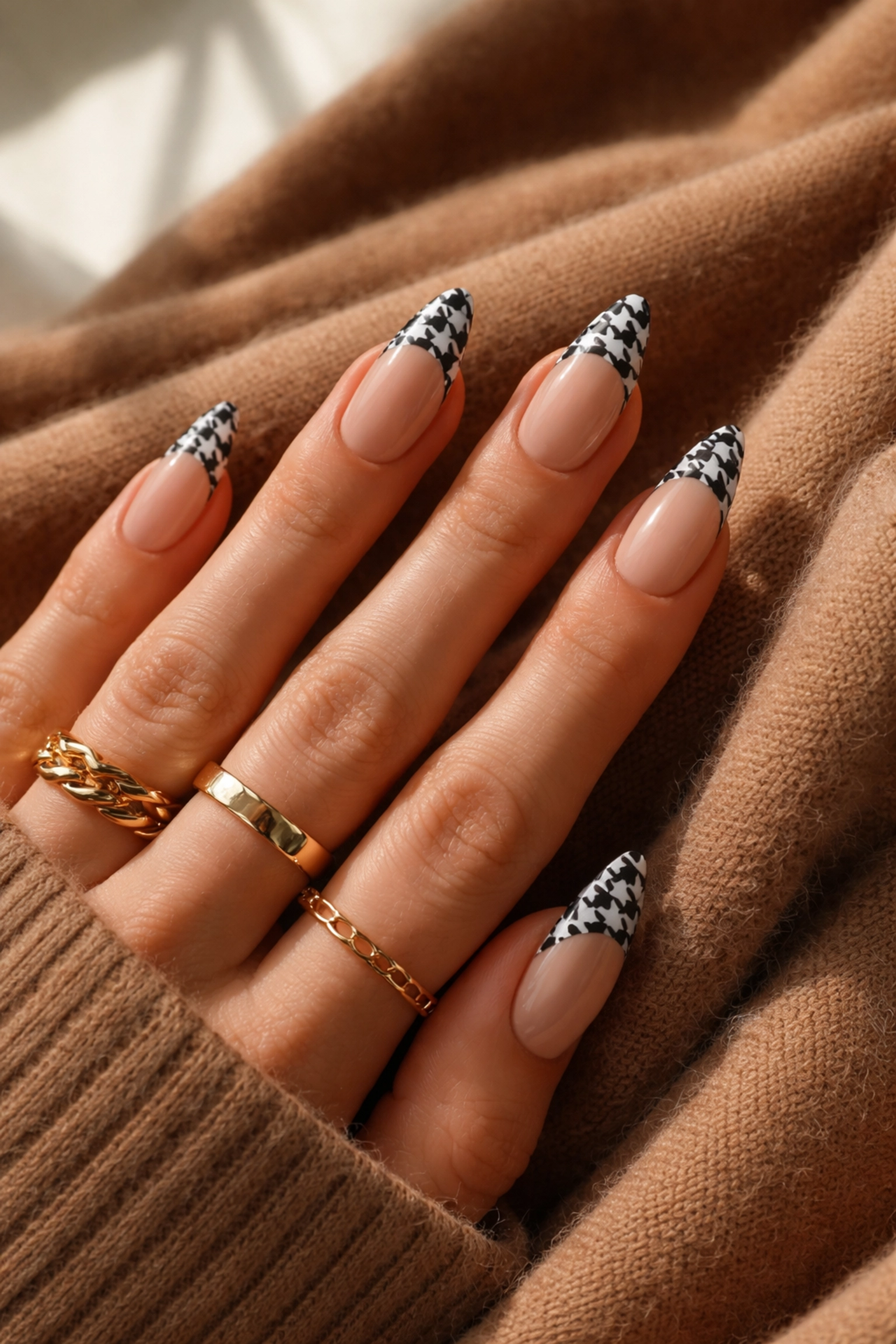 Chic houndstooth French tip nails resting on a cashmere sweater, showcasing trendy nail art for Dedham and Norwood clients.
