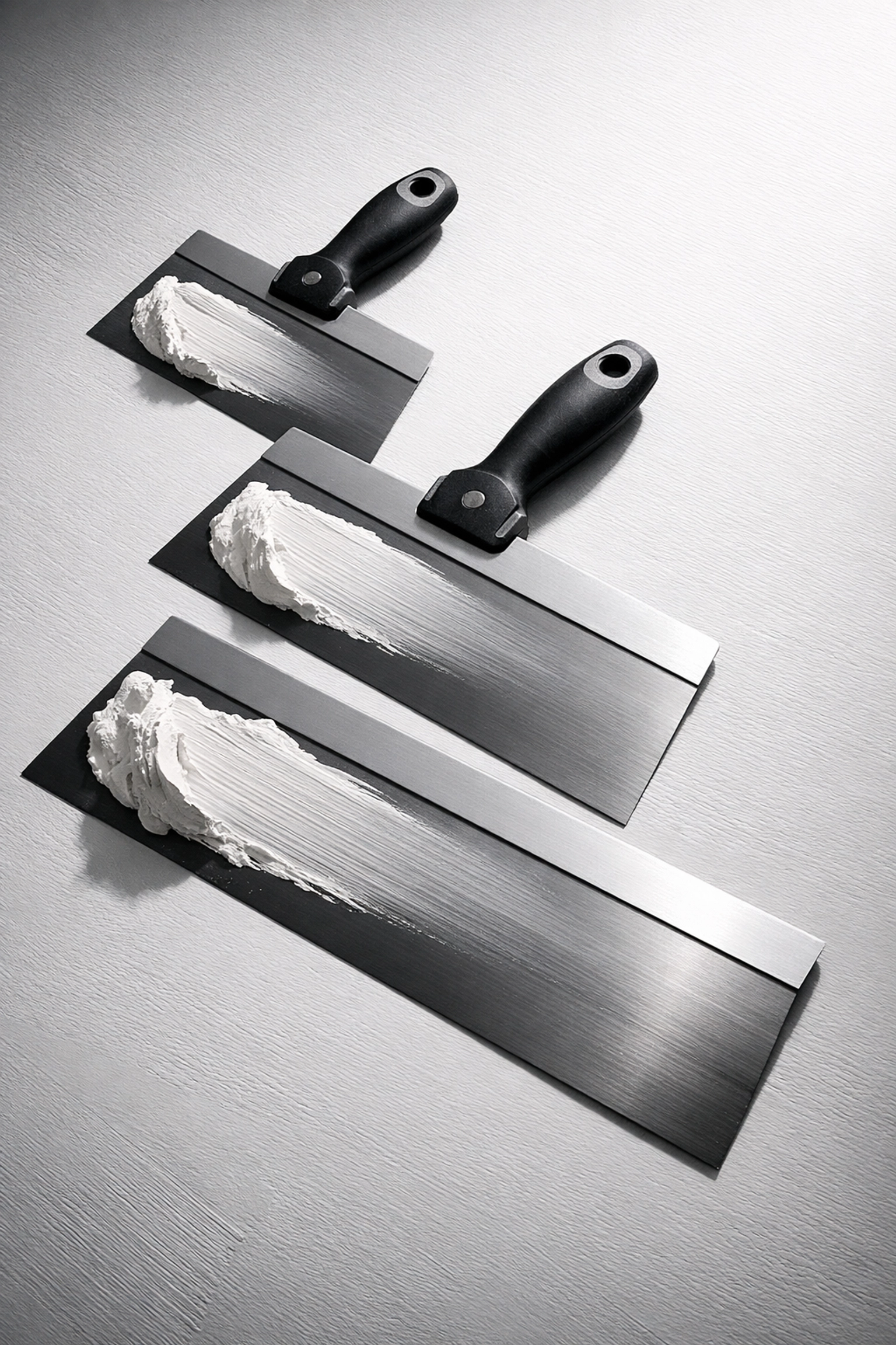 Three drywall knives showing pressure control technique from thick to feathered edge