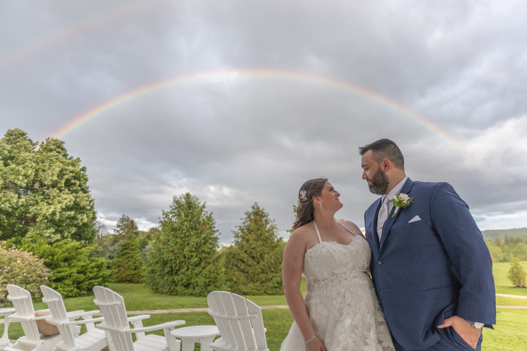 Natalie and Pat standing close together beneath a vibrant rainbow at Olde Homestead