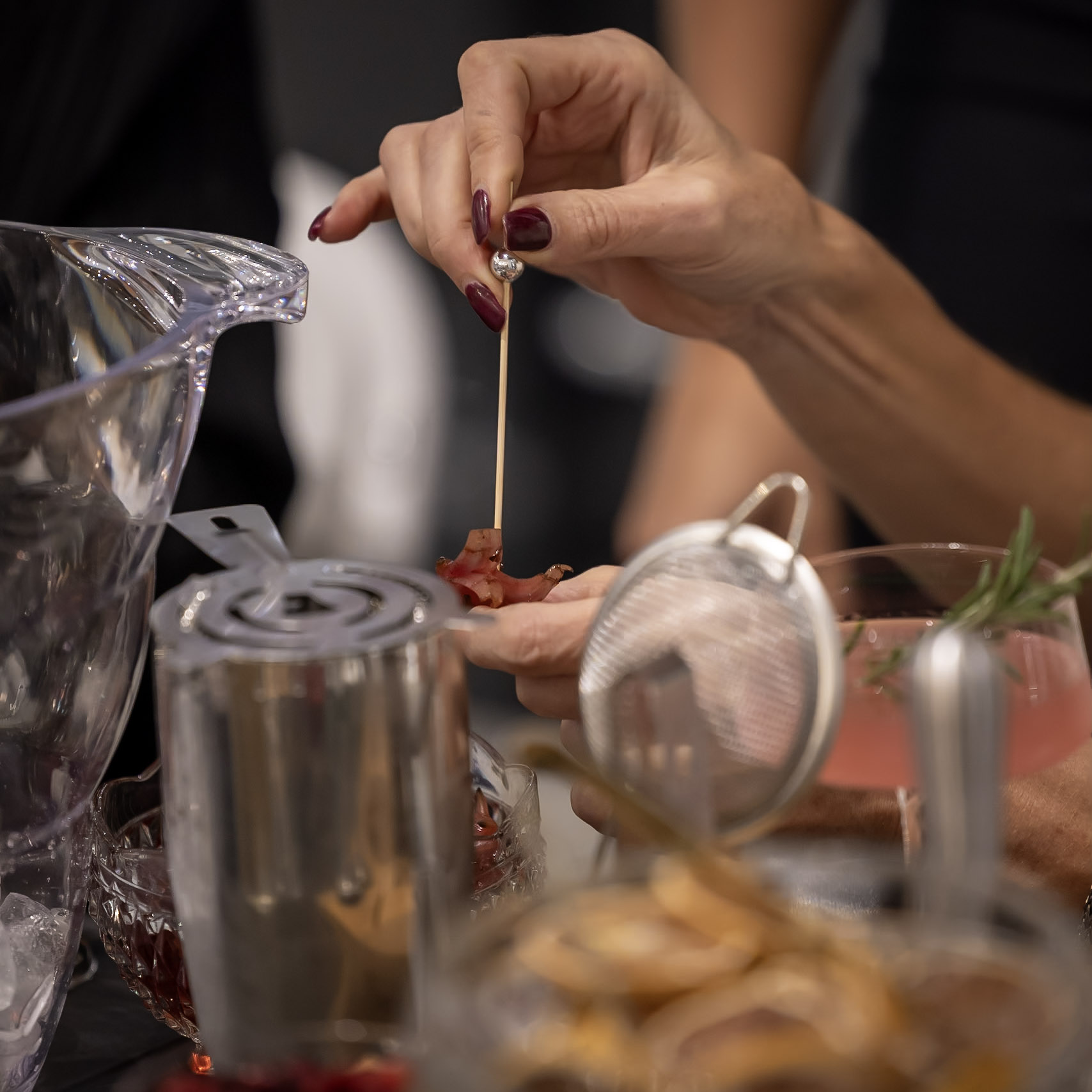 A bartender garnishes a cocktail using a skewer and fresh ingredients