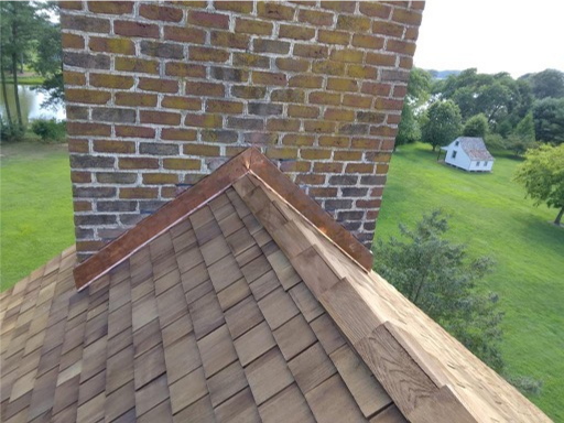 Close-up of a newly installed wood shingle roof with custom copper flashing for a brick chimney
